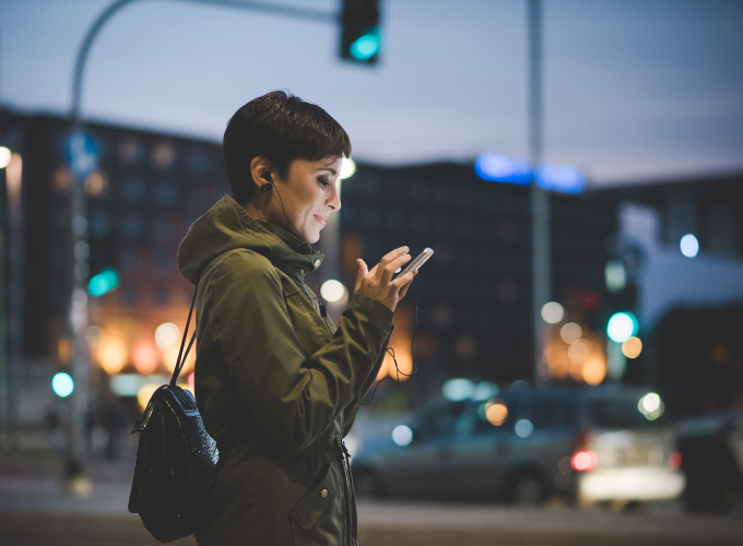 A woman is standing on a city street looking at her cell phone.