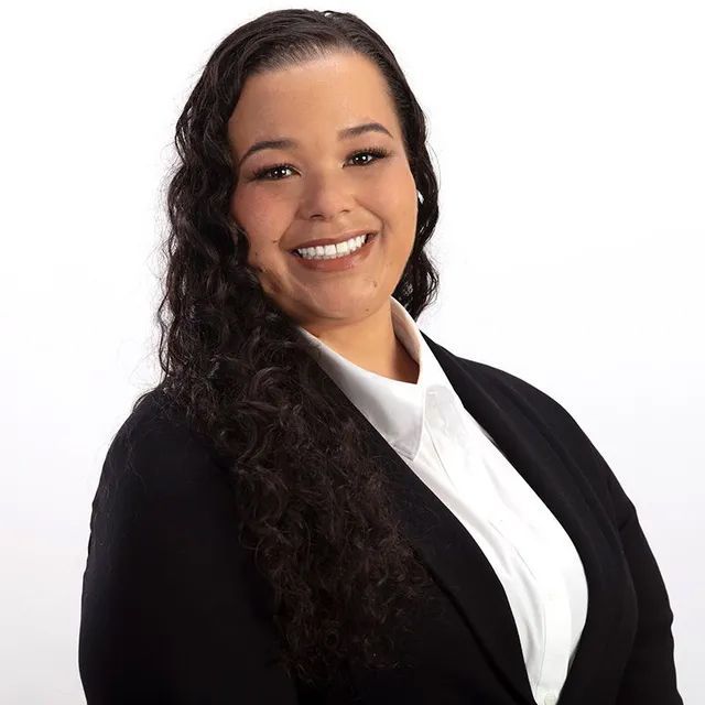 A woman wearing a black jacket and white shirt is smiling for the camera.