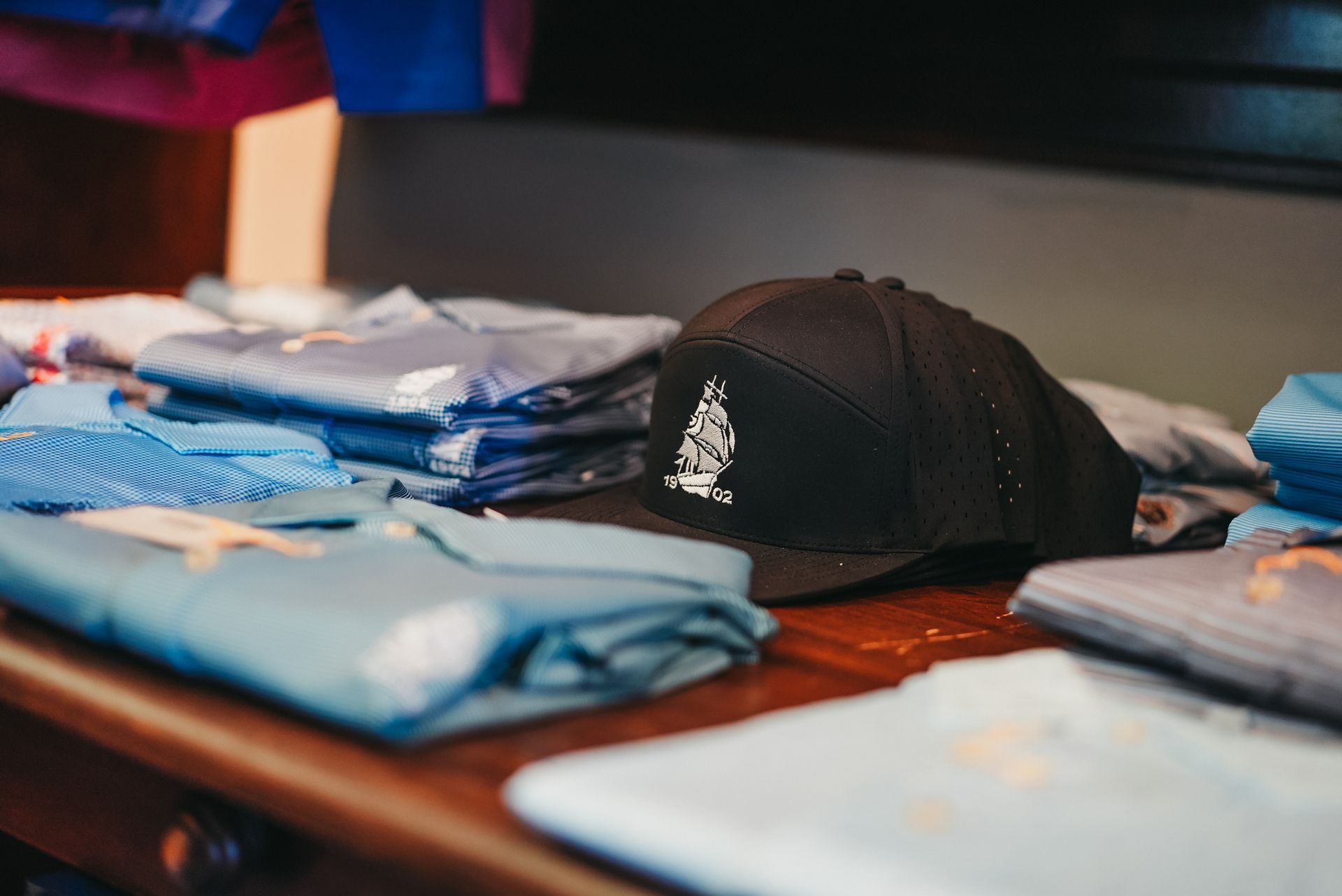 Black cap with white logo on a table with folded blue shirts.