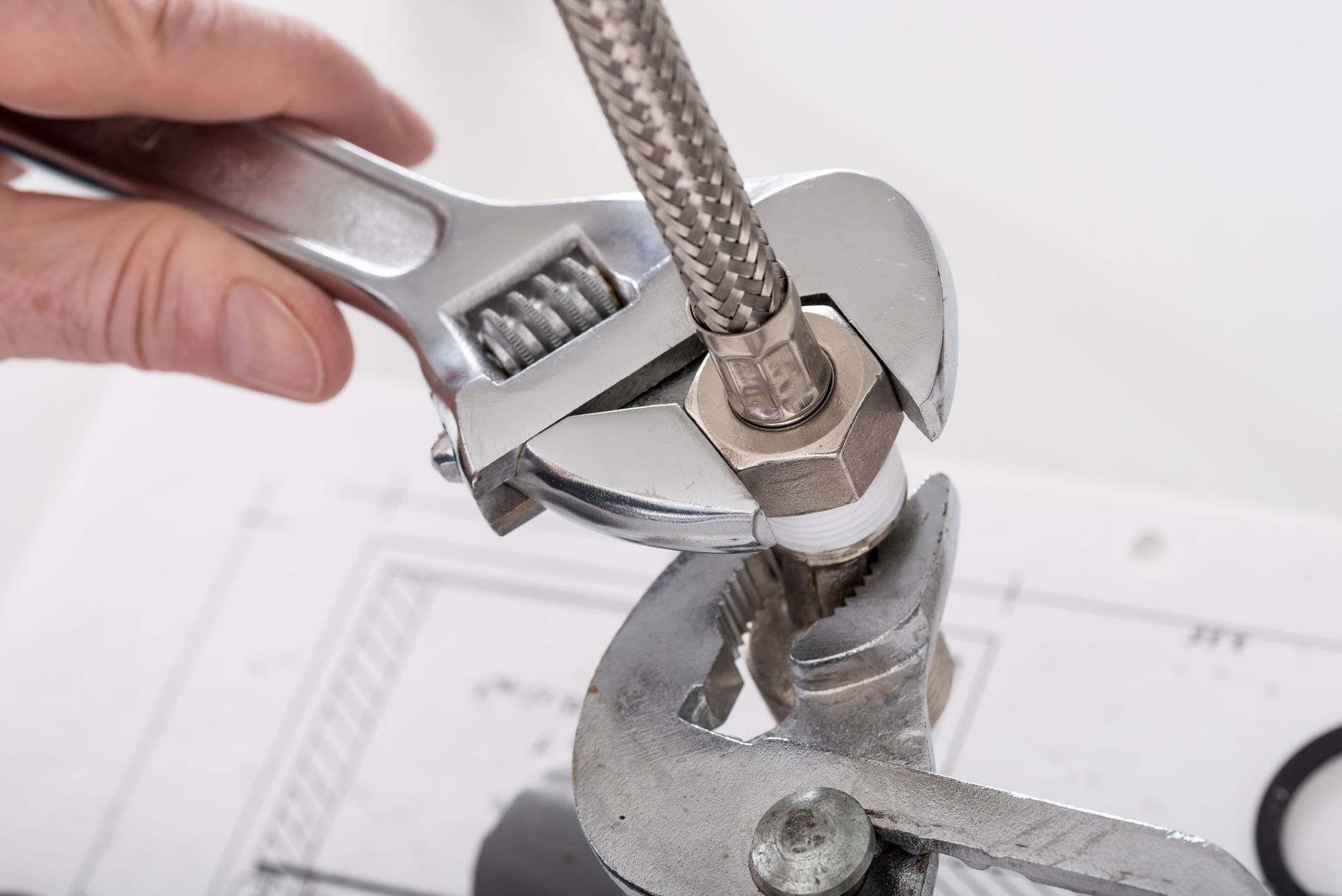 A hand using an adjustable wrench to tighten a chrome faucet hose fitting on a sink.