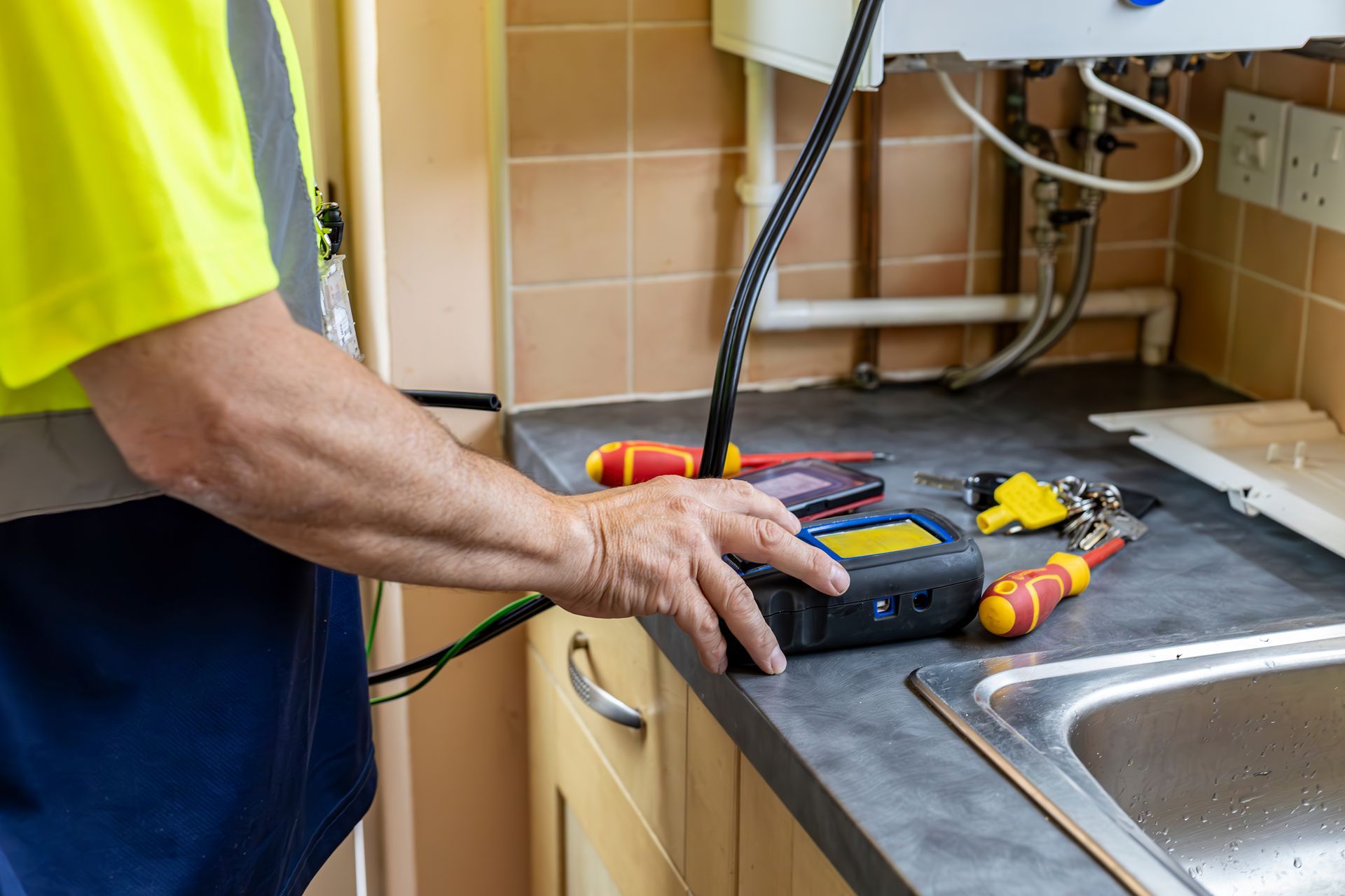 Technician using a multimeter to test a kitchen sink drain pipe under the counter
