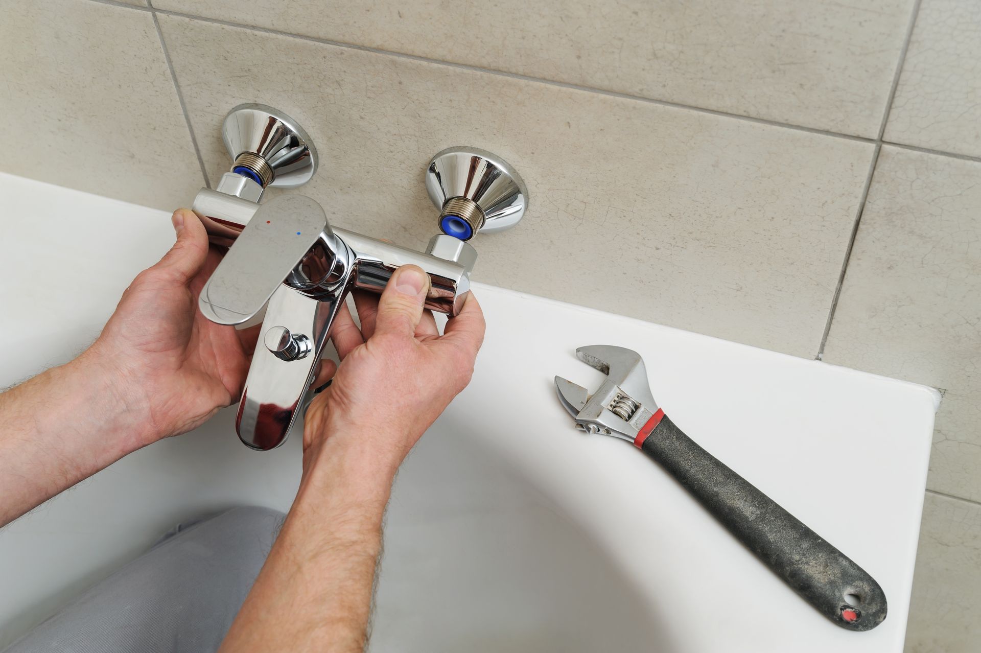 Hands installing chrome bathroom faucet with wrench beside sink