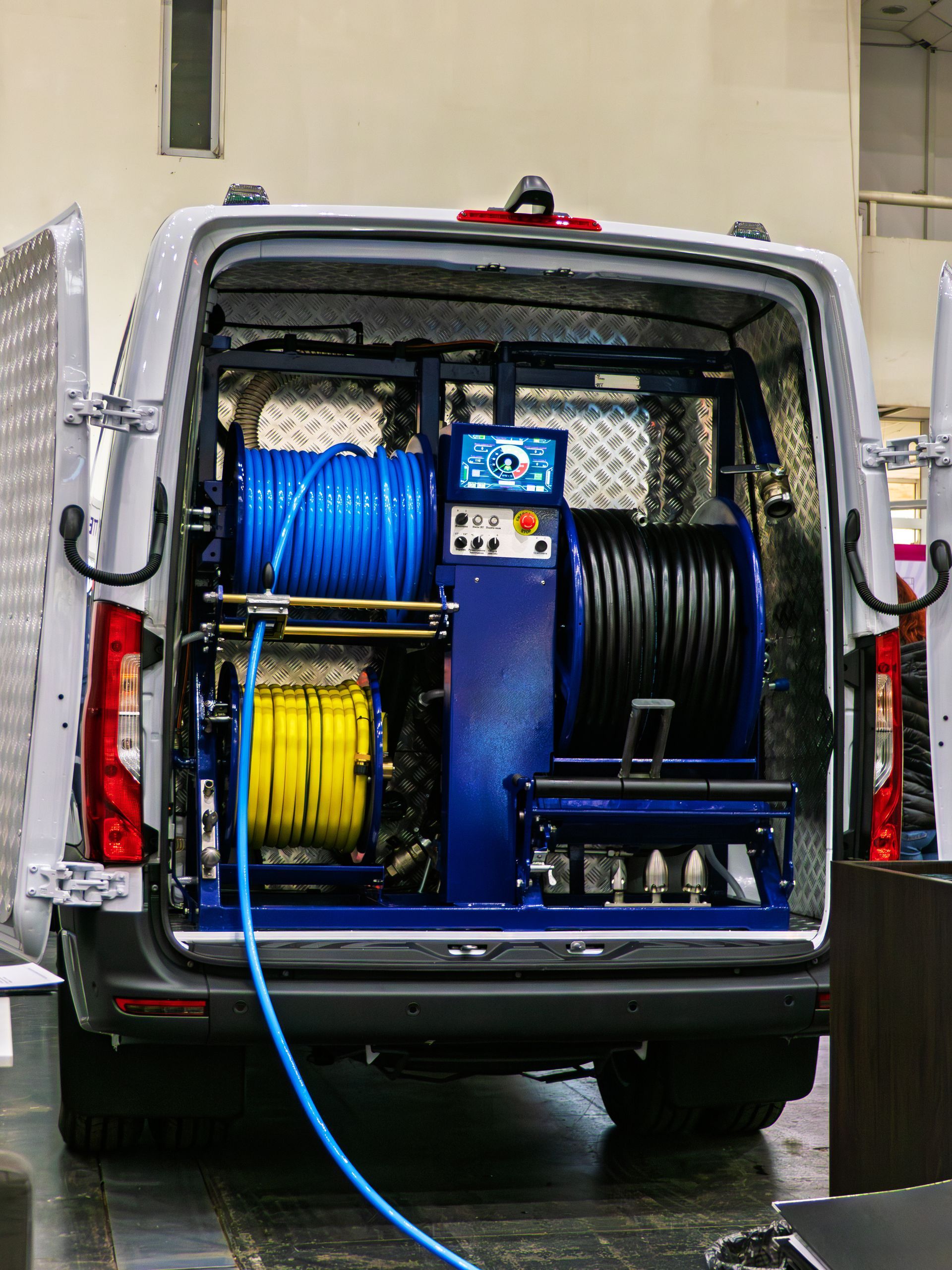 Service van with open rear door showing large blue and black hose reels and cleaning equipment