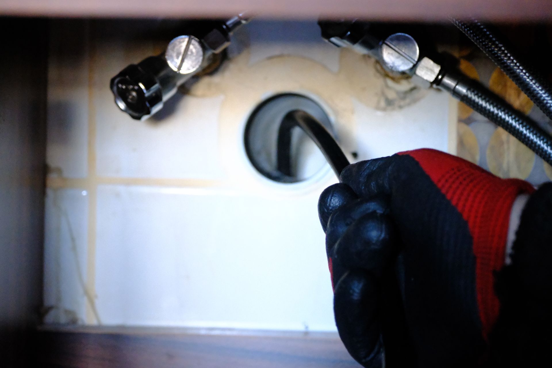 Gloved hand connecting a hose to a wall fitting with two metal connectors nearby