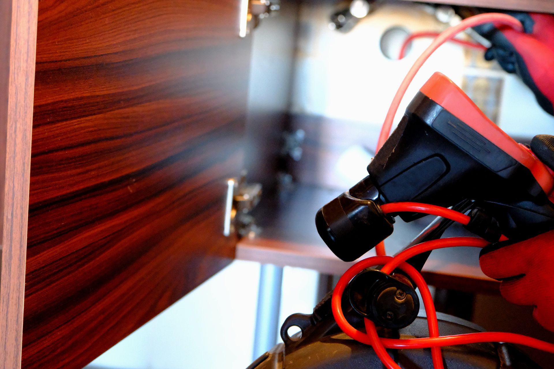 Close-up of a worker drilling near red wiring inside an electrical panel
