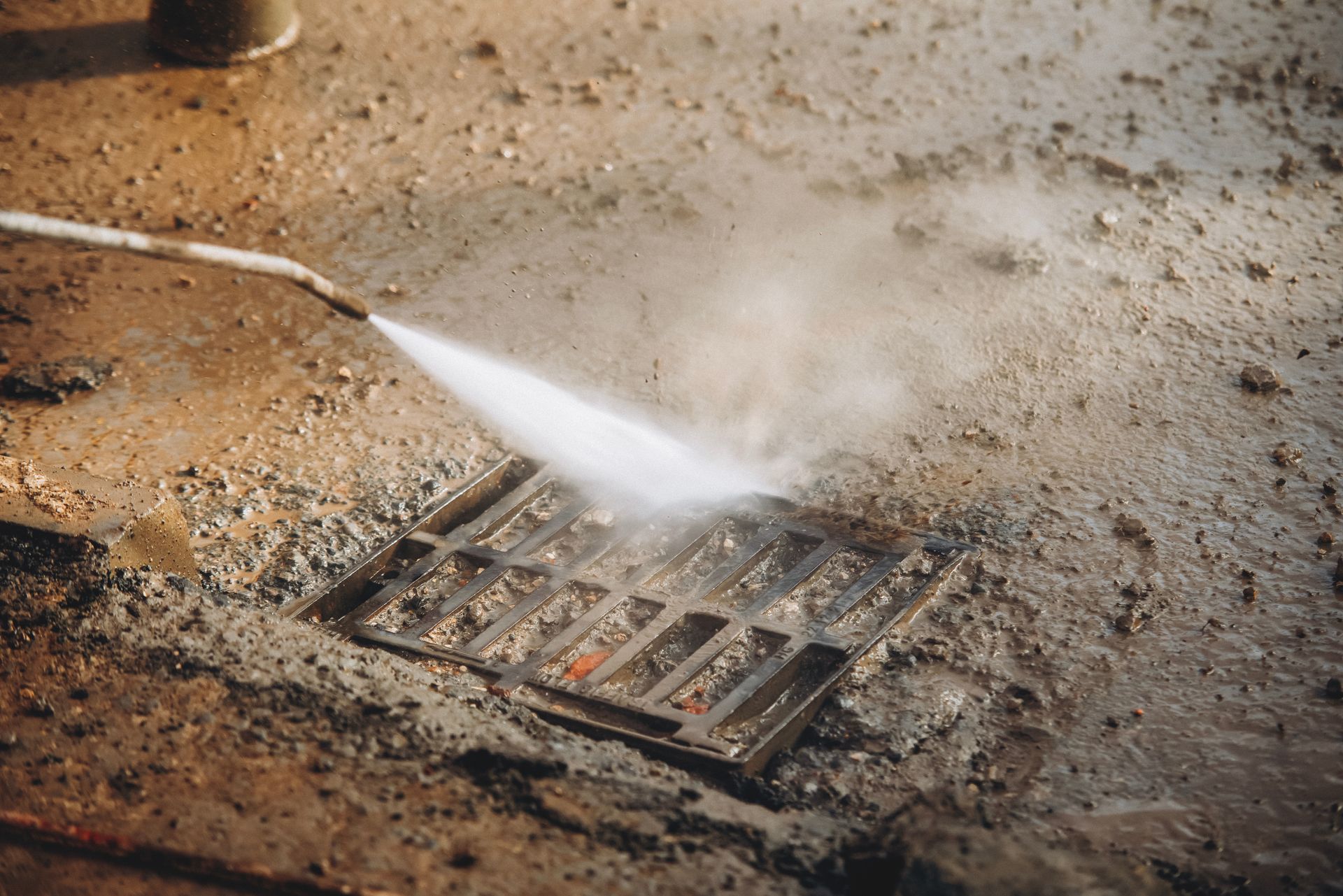 Pressure washer spraying a dirty metal drain grate on wet ground