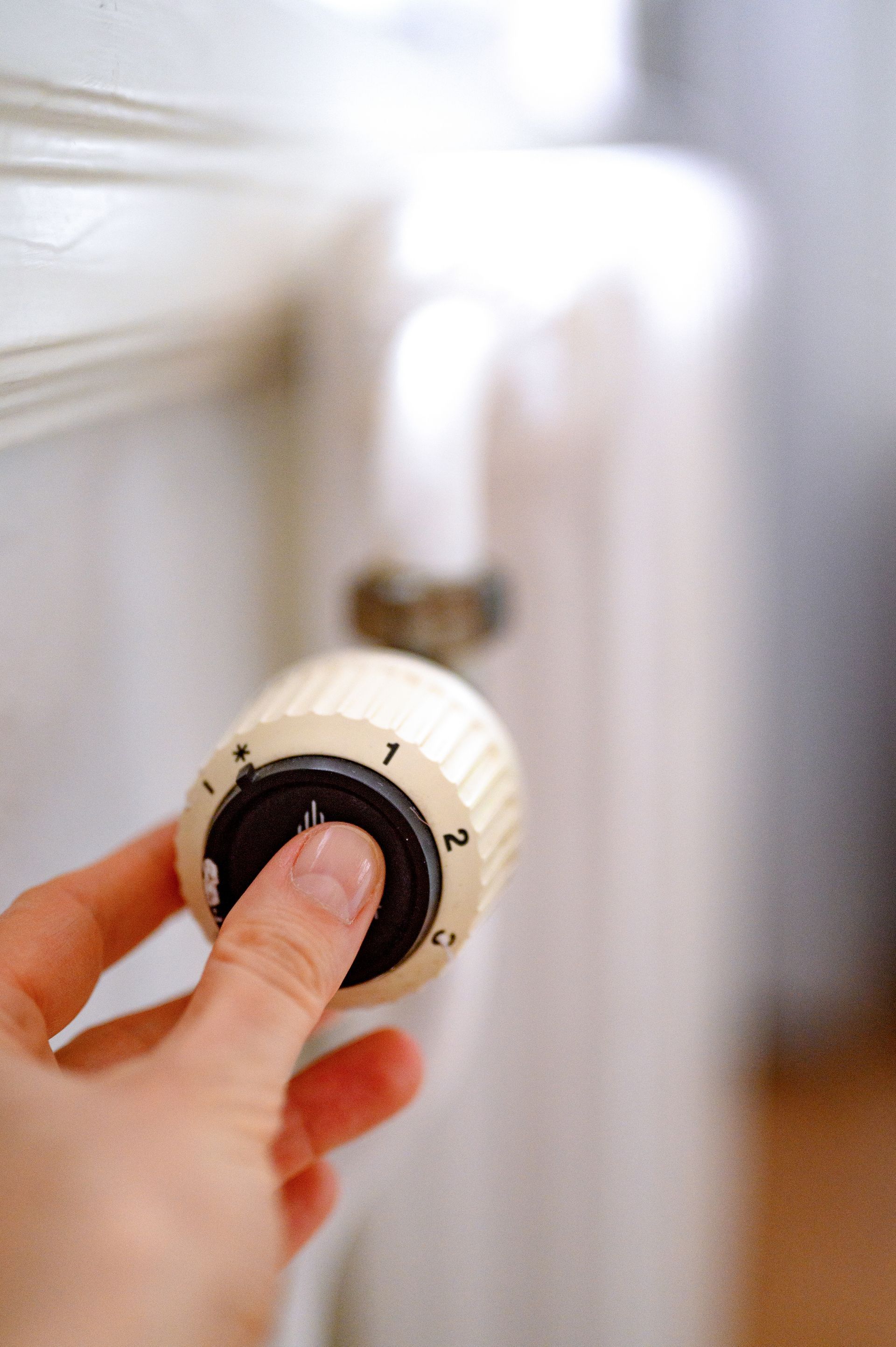 Hand turning a white radiator thermostat dial in a bright room
