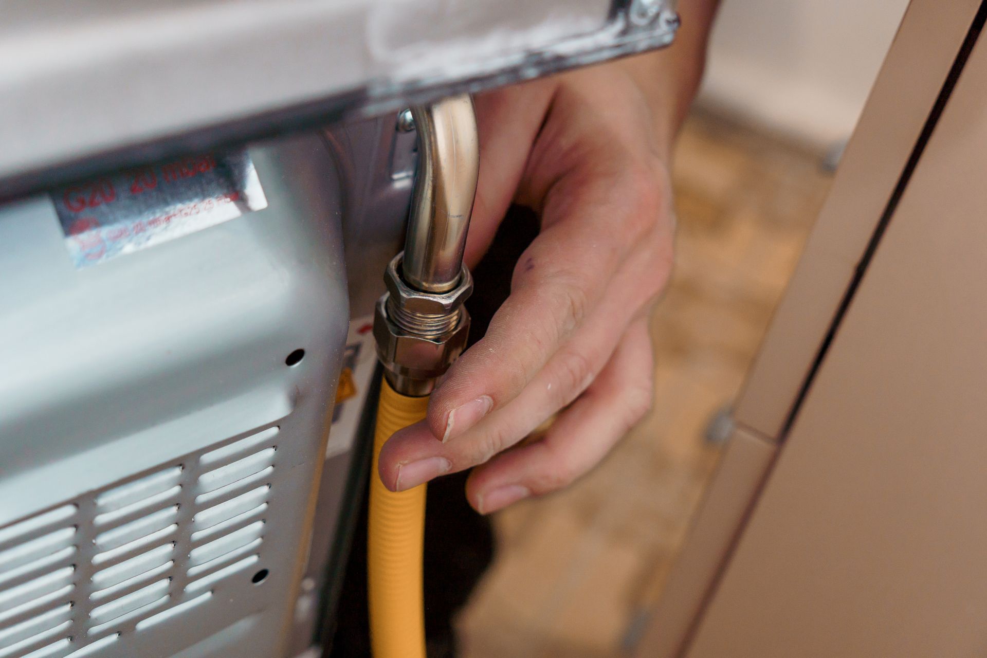 Hand connecting a yellow gas hose to an appliance valve with a wrench.