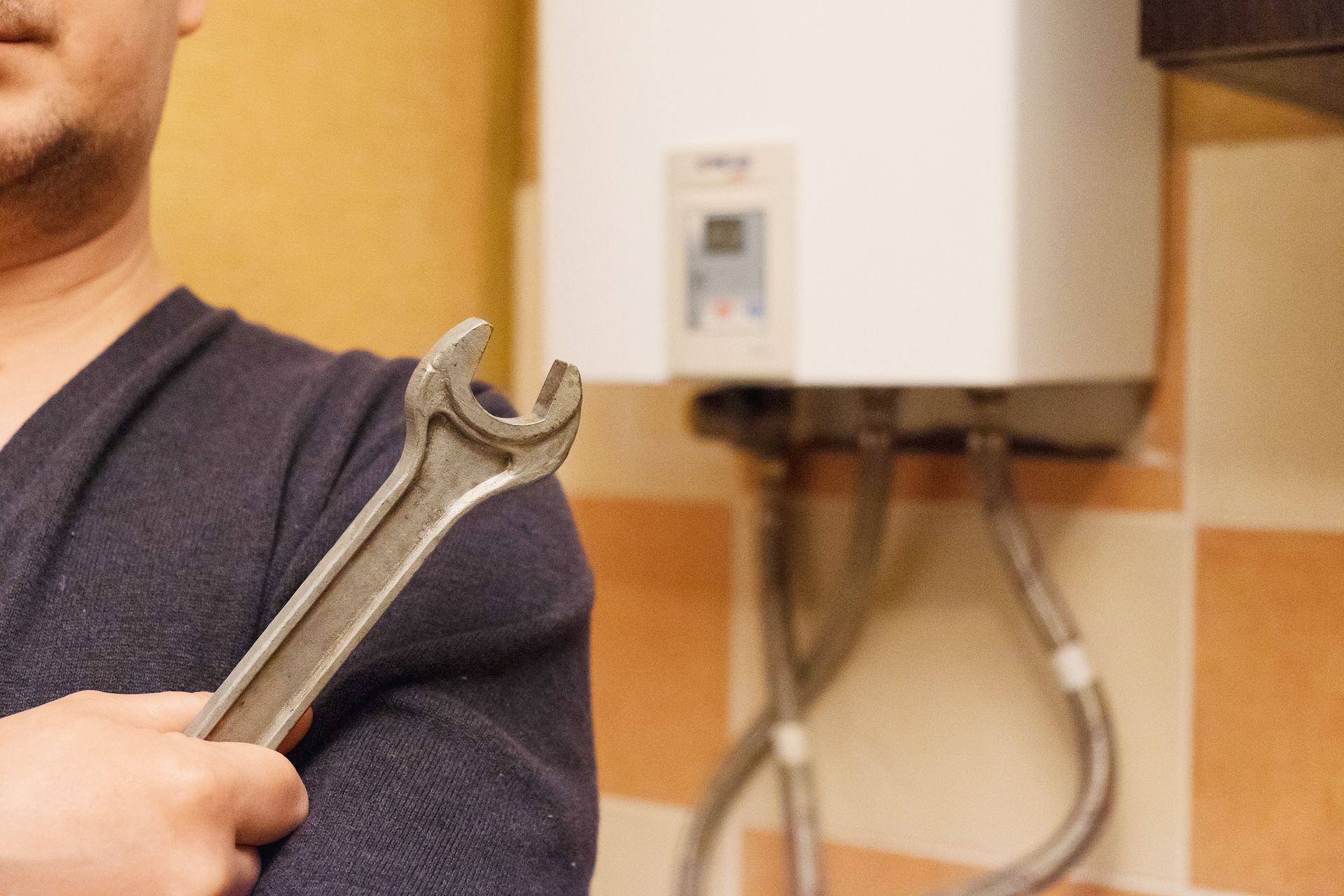 Person holding a wrench near a wall-mounted boiler or water heater