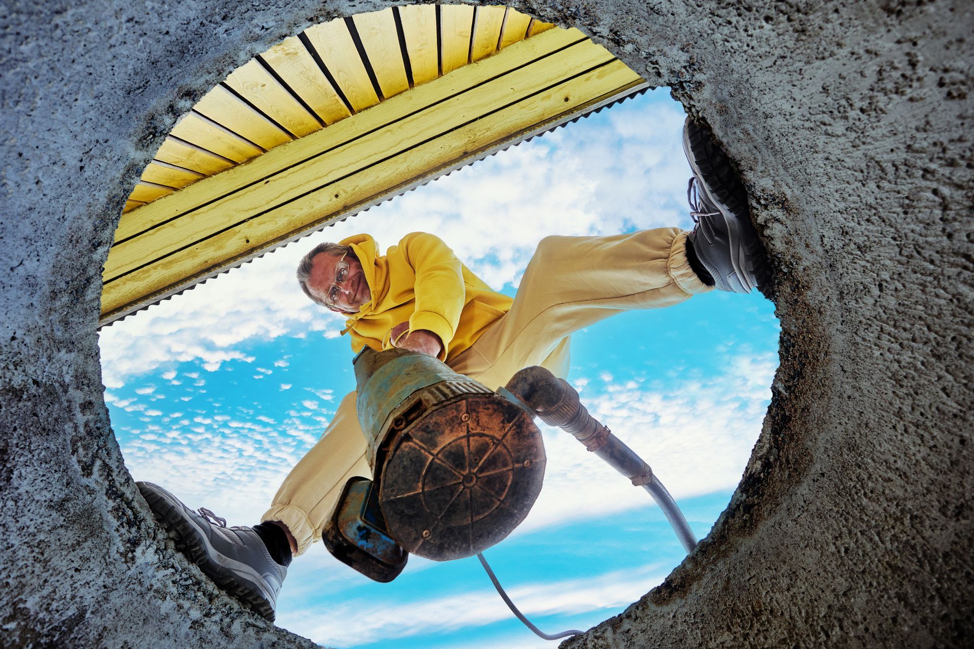 Person leaning over a well opening, using a bucket and rope against a blue sky.