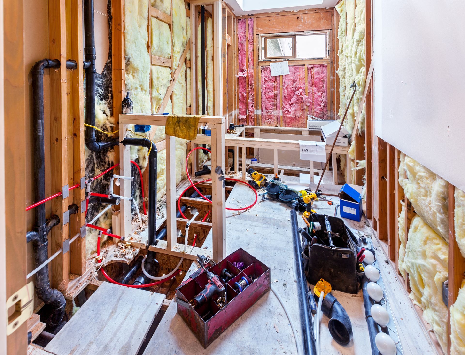 Bathroom under renovation with exposed plumbing, insulation, tools, and construction materials