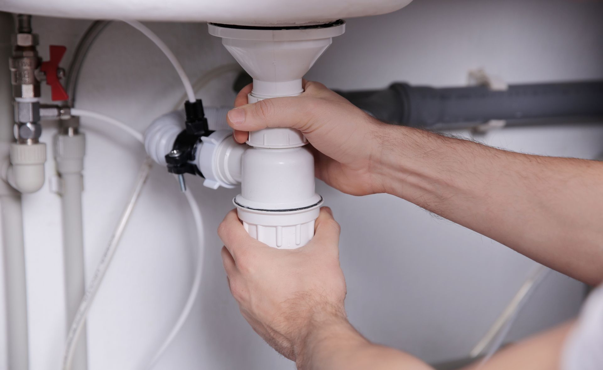 Hands adjusting a chrome sink faucet with pliers in a bright kitchen sink area