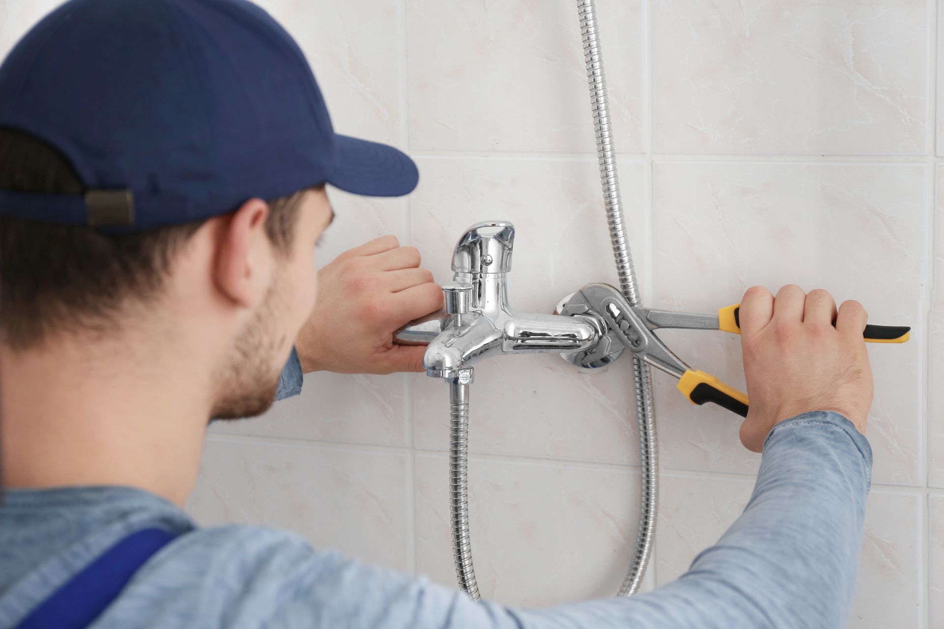 Plumber installing a chrome shower fixture on a tiled bathroom wall with a wrench