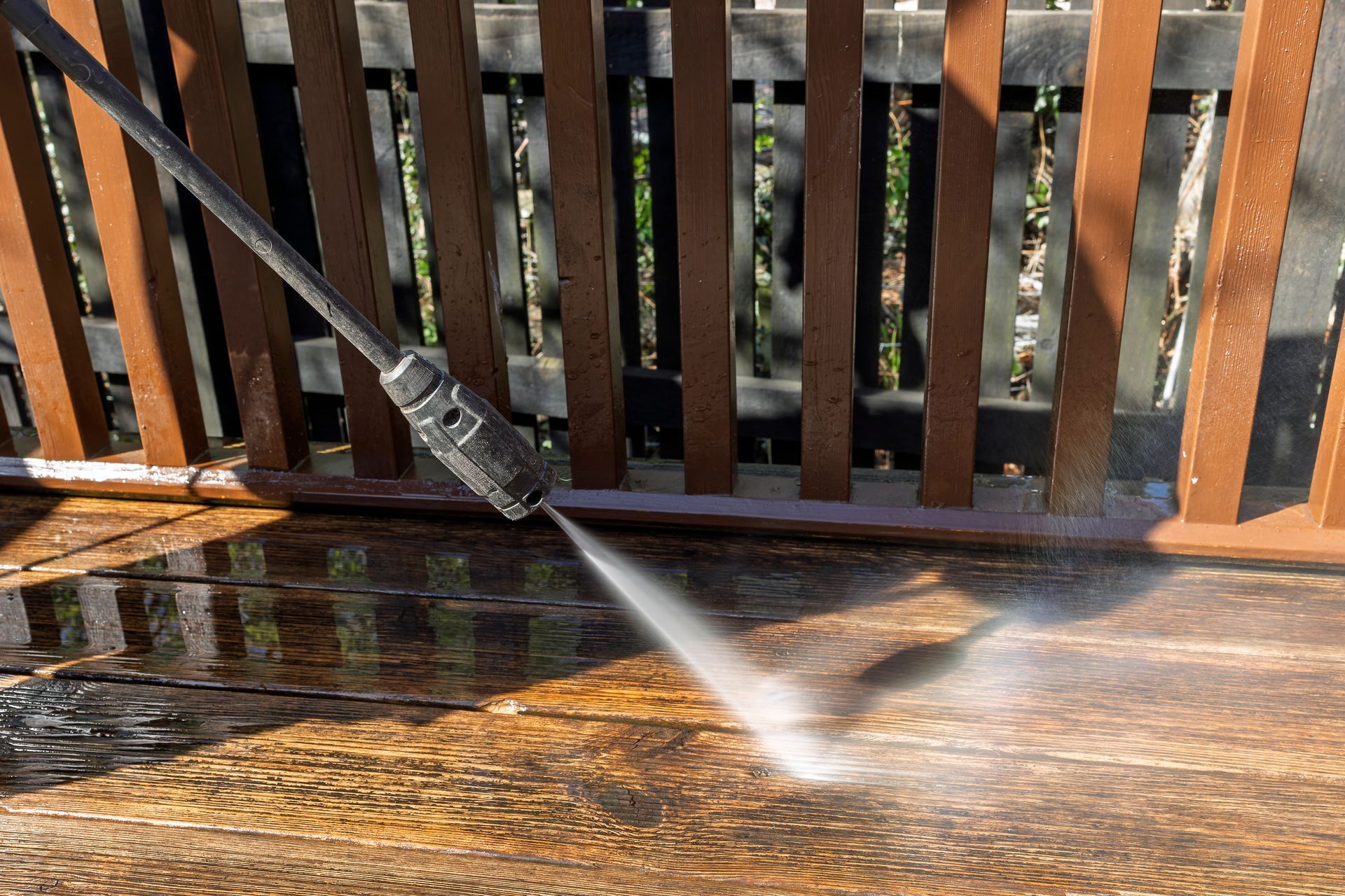 Person pressure-washing a wet wooden deck with a high-pressure spray nozzle