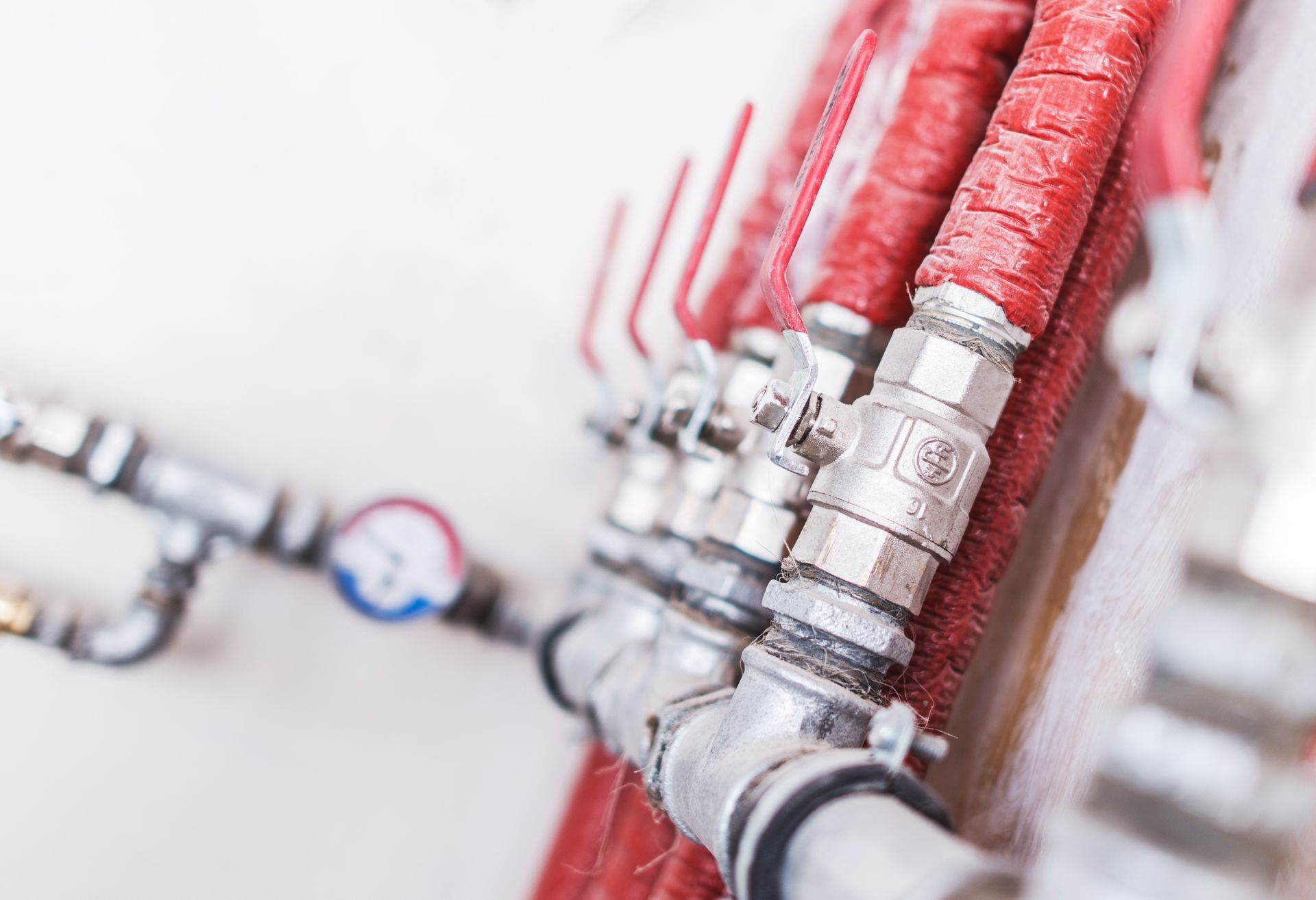 Red pipes and metal valves on a white wall in a close-up plumbing system view