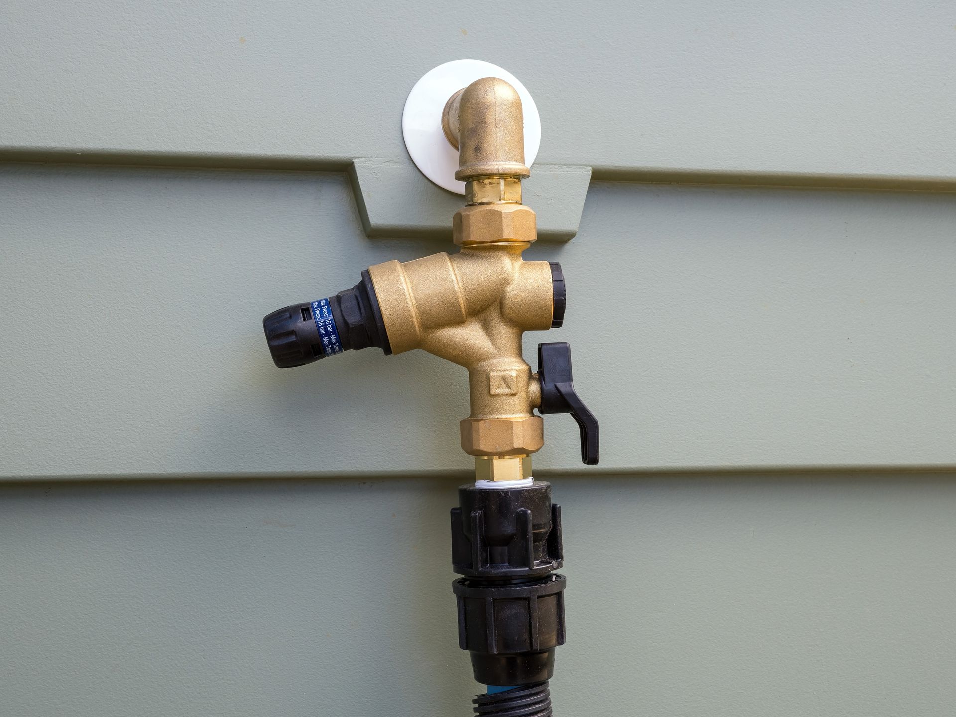 Brass garden hose sprinkler valve on a gray siding wall