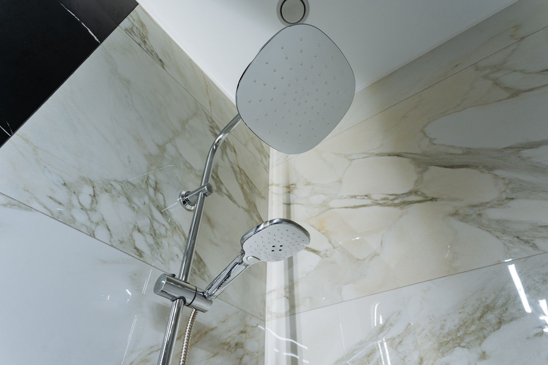 Modern shower with chrome fixtures and marble-patterned wall tiles