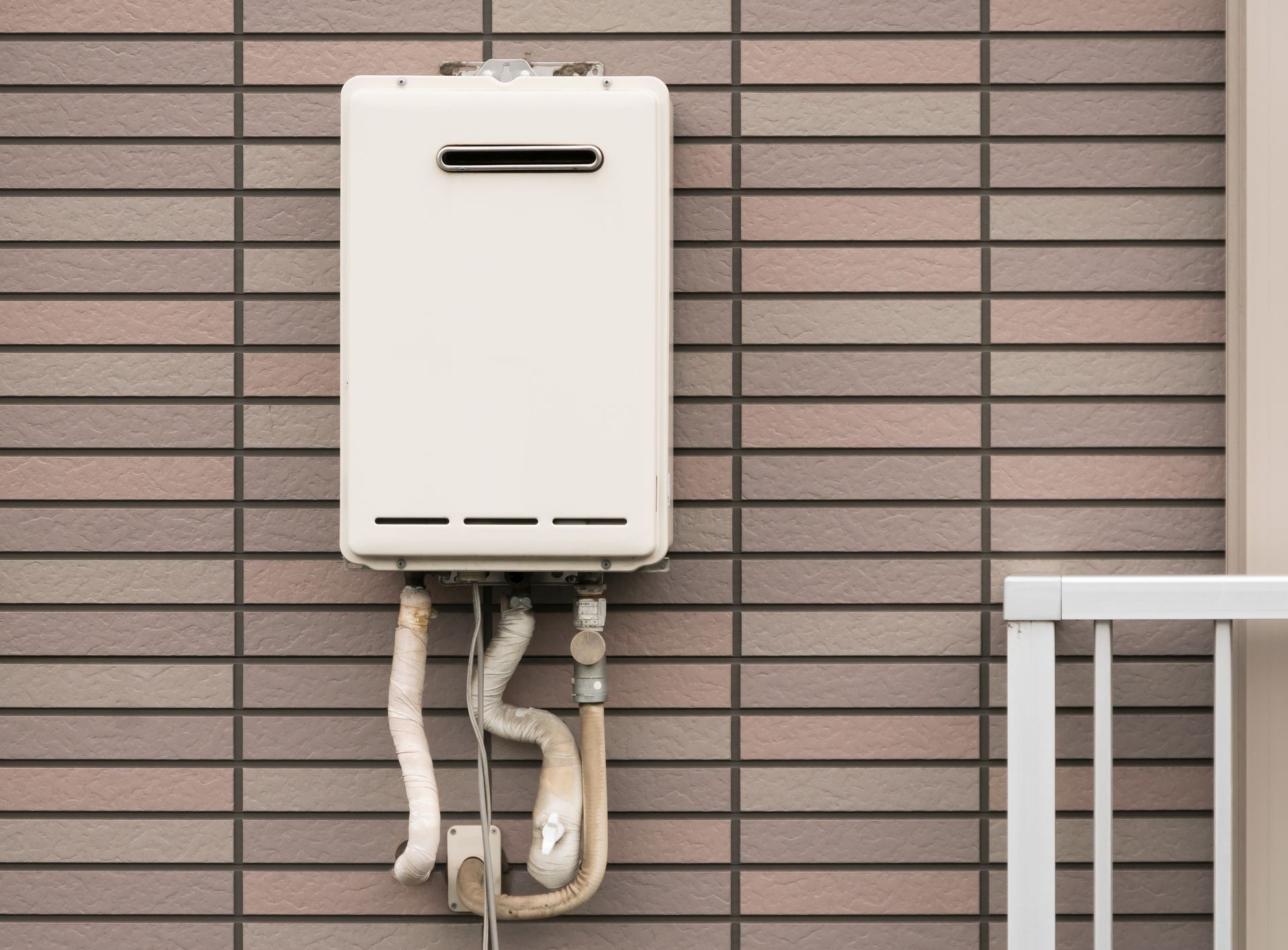 White wall-mounted utility box with pipes on a tiled exterior wall near a railing