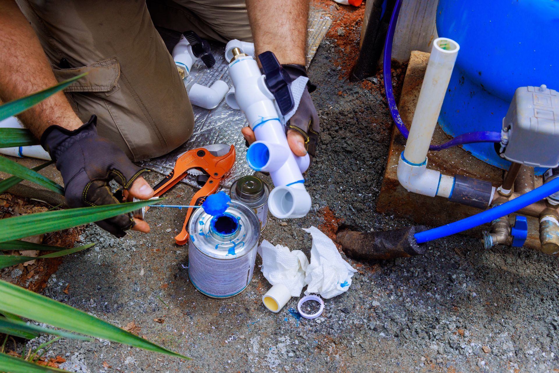 Technician repairing PVC plumbing pipes with blue primer and tools on gravel ground