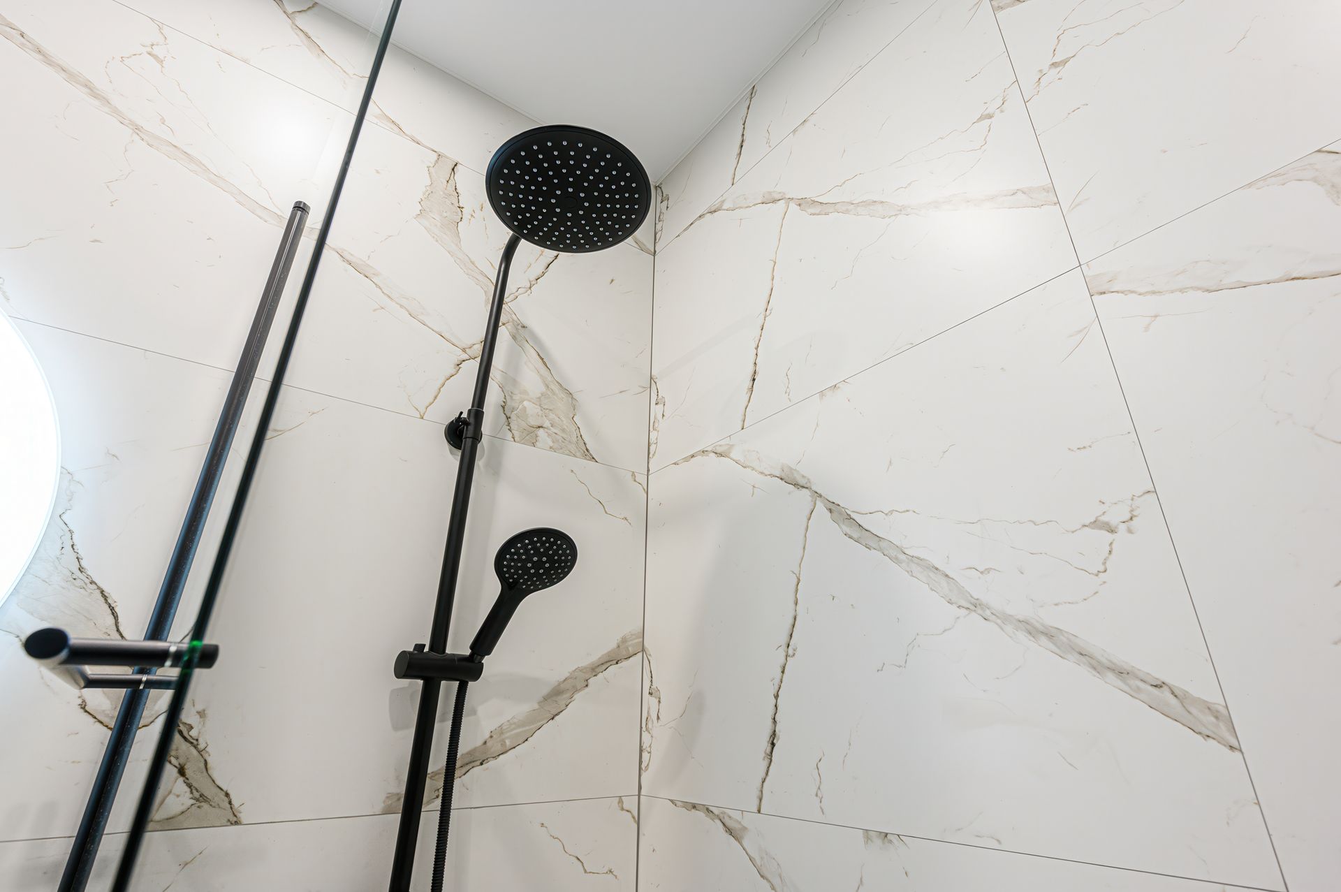 Black shower heads and chrome rails in a white tiled shower stall.