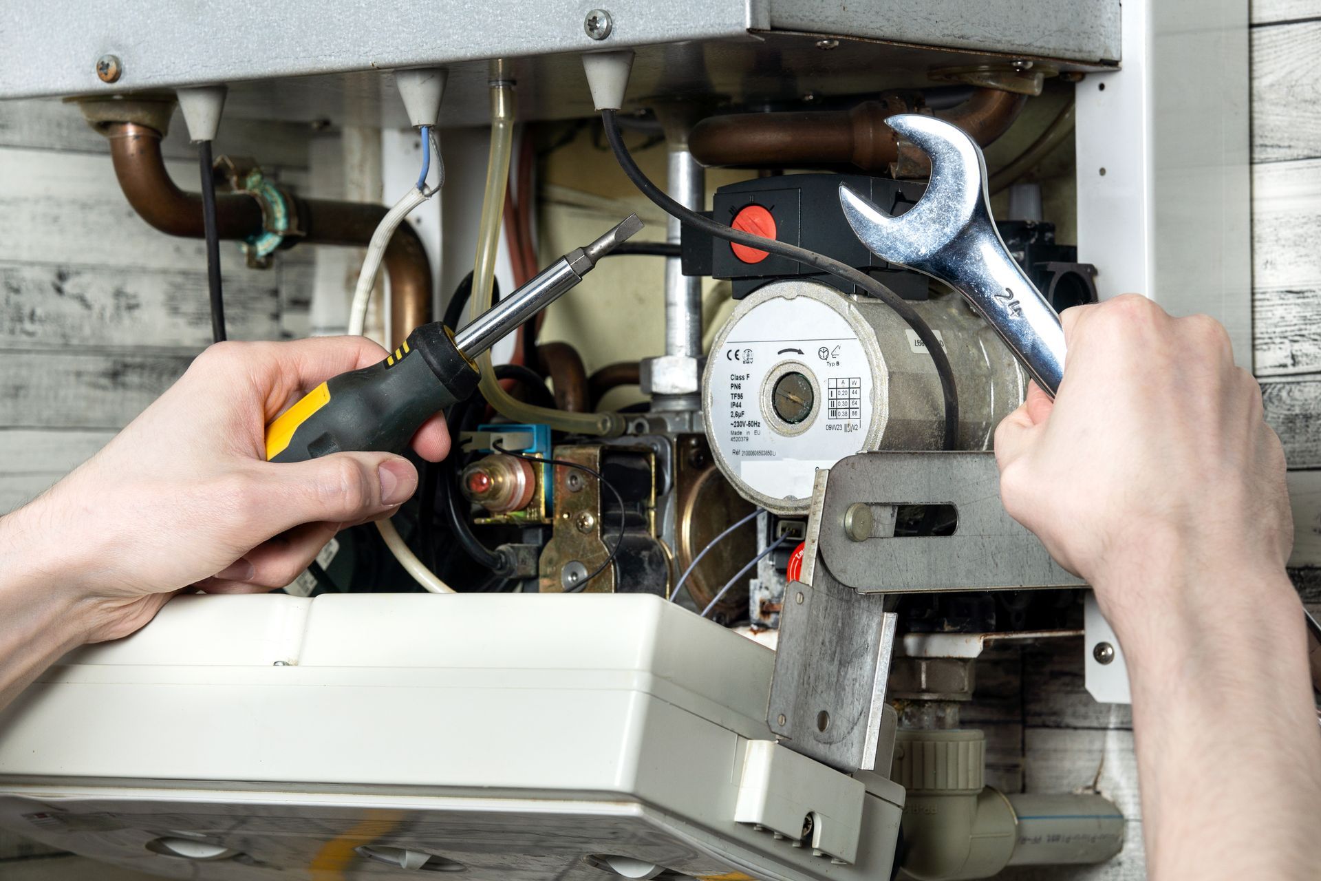Hands using pliers and a screwdriver to repair the inside of a boiler unit