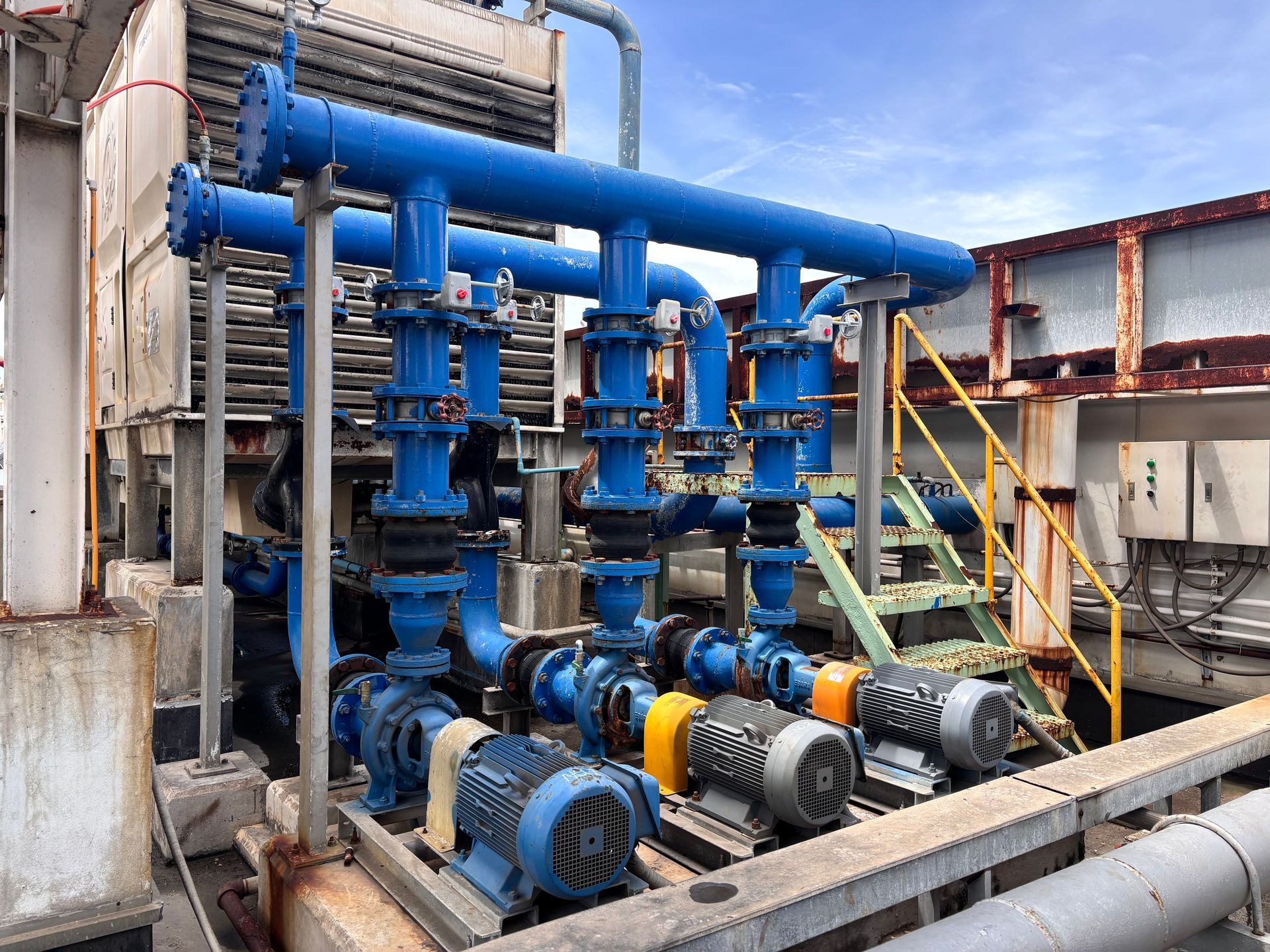 Industrial pump and pipe system with blue motors, valves, and yellow handrails in a factory setting