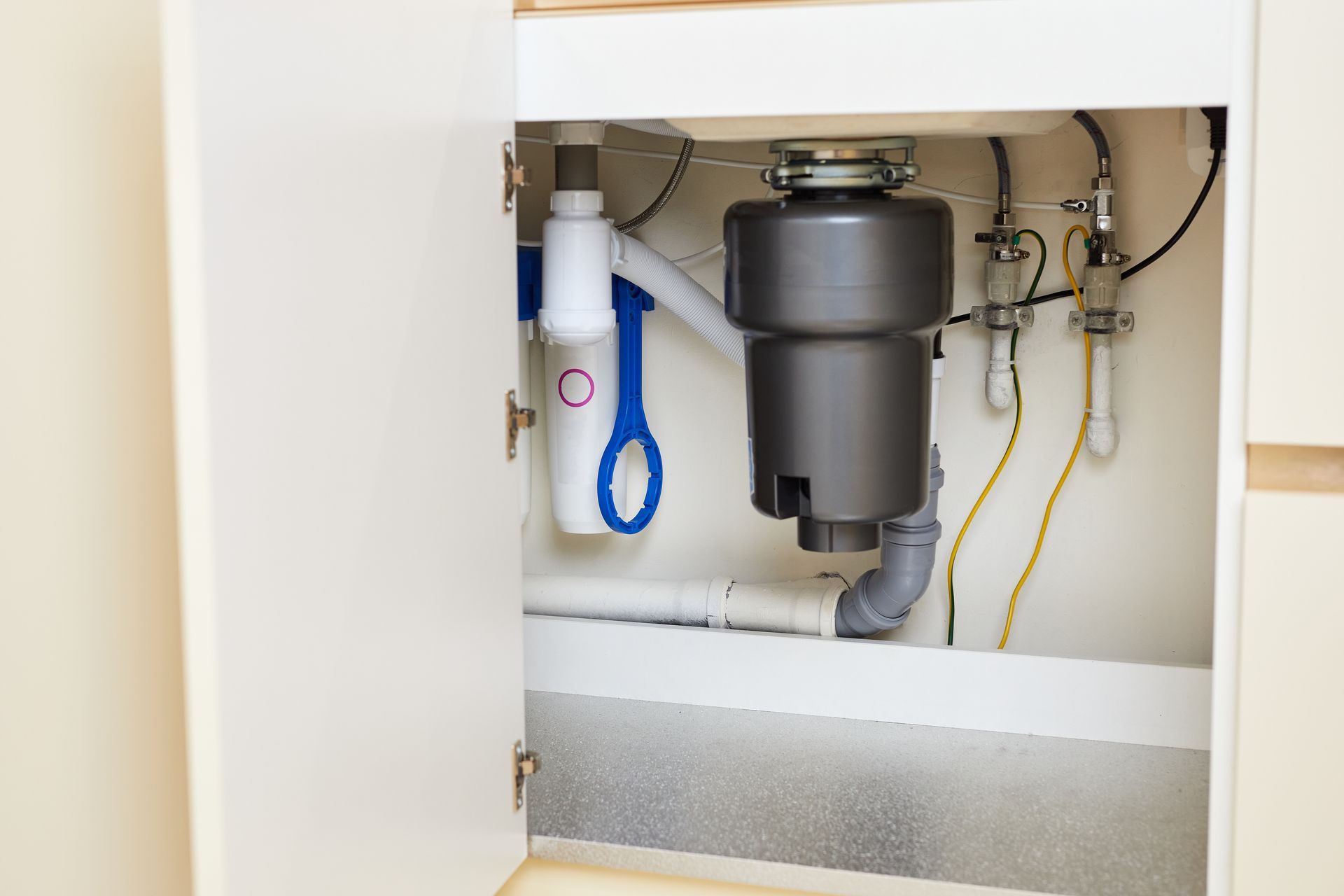 Open cabinet with plumbing and under-sink filtration system, white interior and blue hose