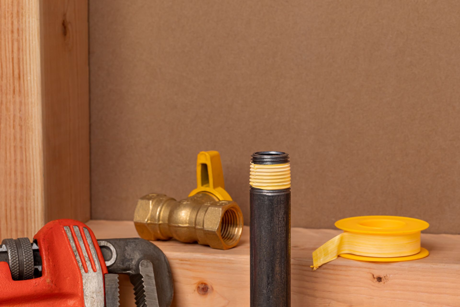 Brass pipe fittings and a yellow tape measure on a wooden shelf