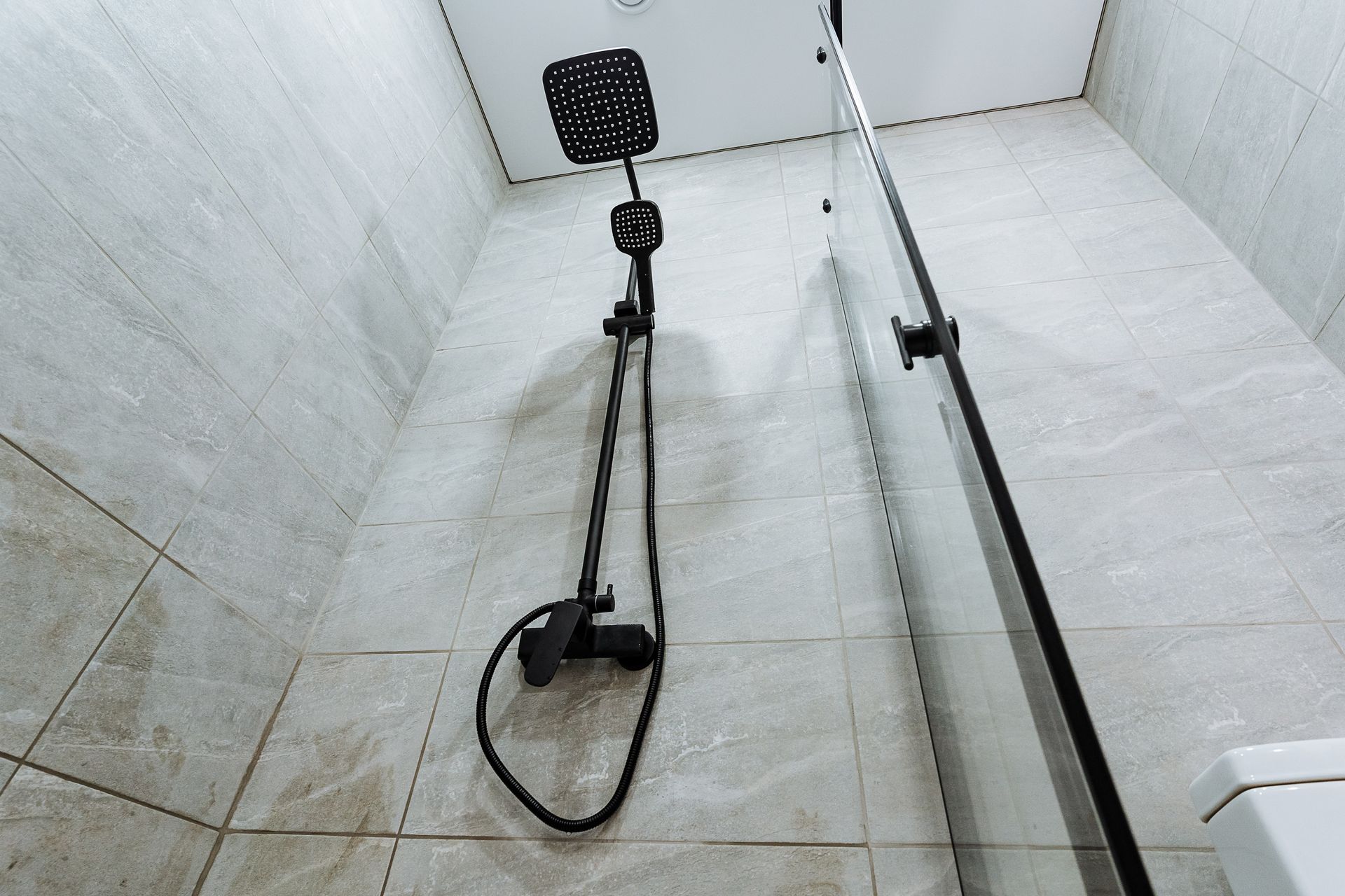 Shower stall with a showerhead, hose, and tiled white walls and floor.