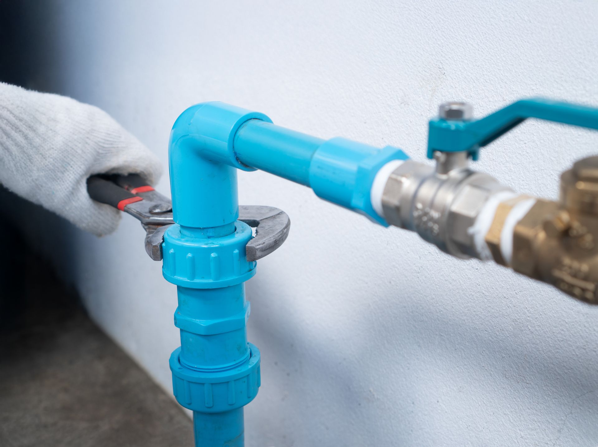 Gloved hand tightening a blue PVC pipe fitting beside a metal valve