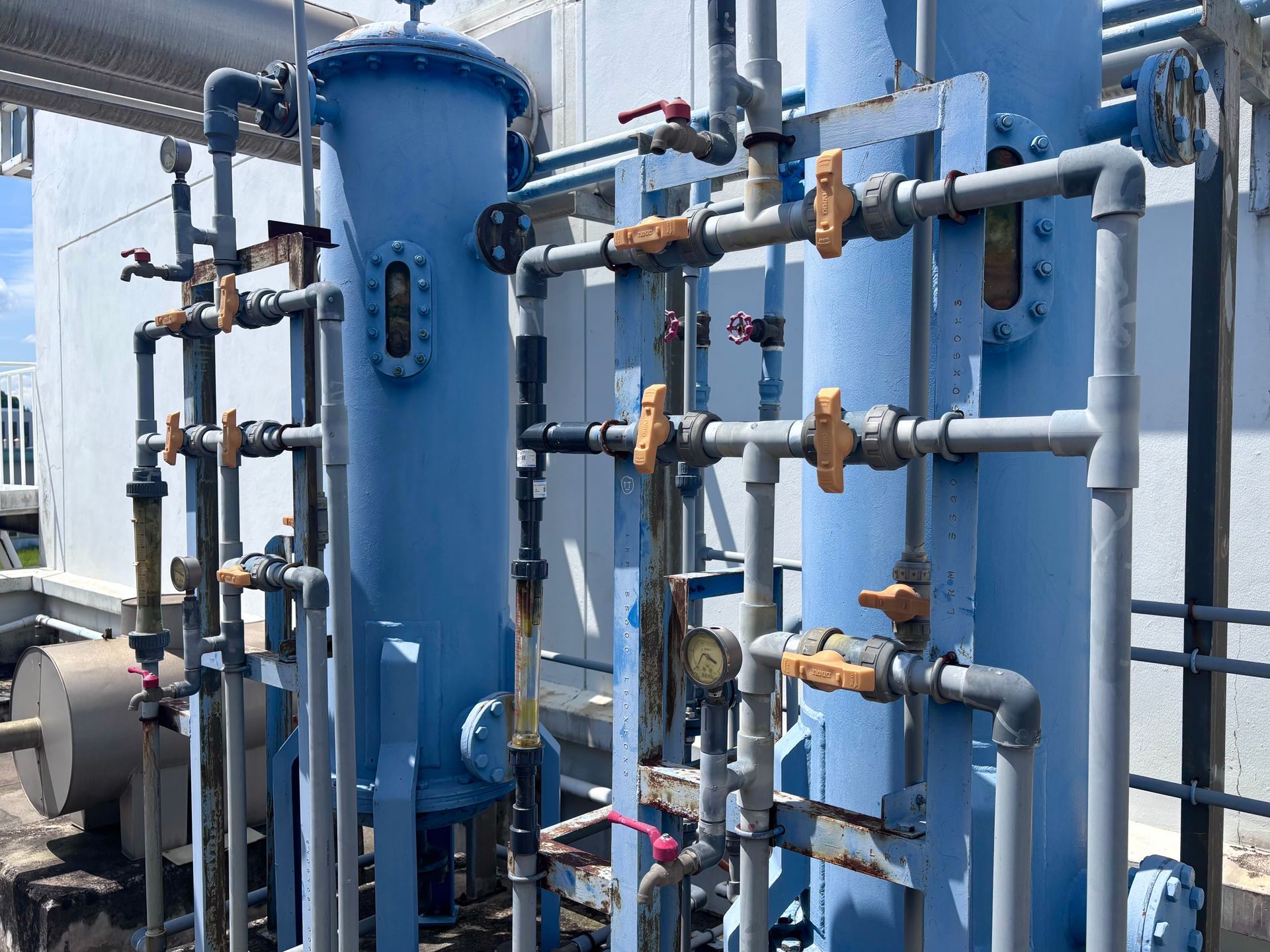 Blue industrial water tank with pipes, valves, and gauges in an outdoor utility area