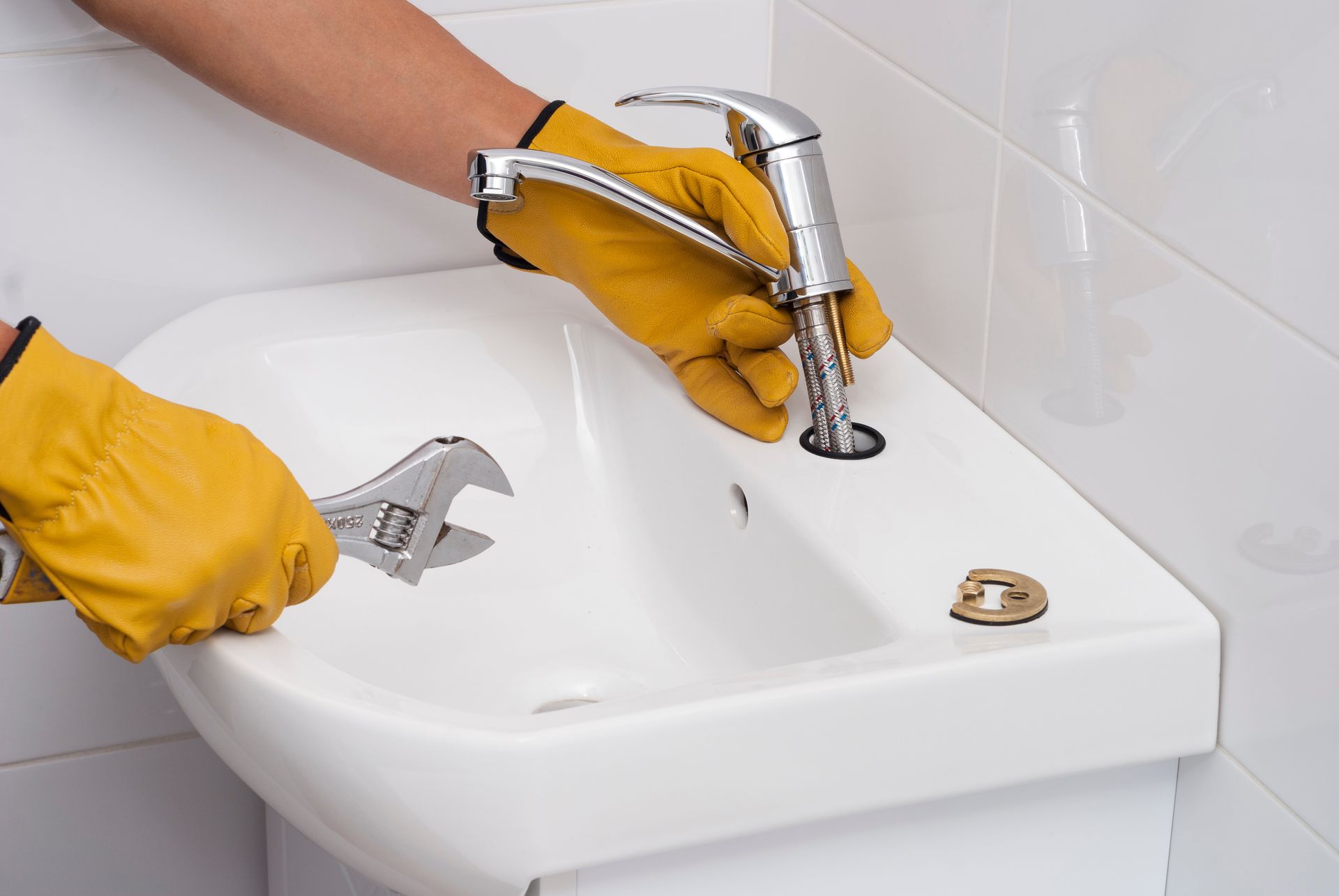 Gloved hands using a wrench to tighten a faucet on a white sink in a bathroom