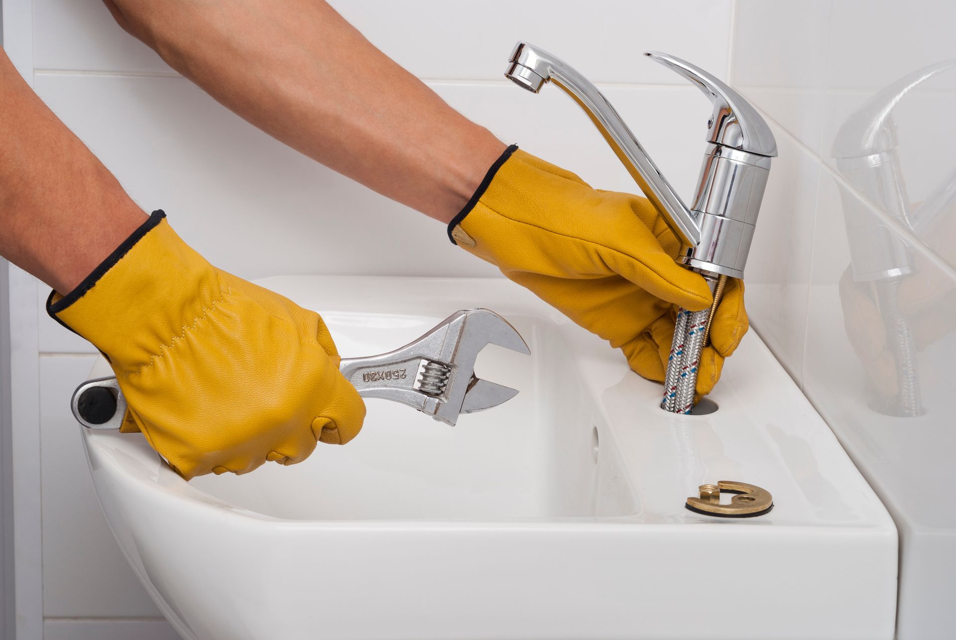 Yellow-gloved hands repairing a bathroom sink faucet with wrenches
