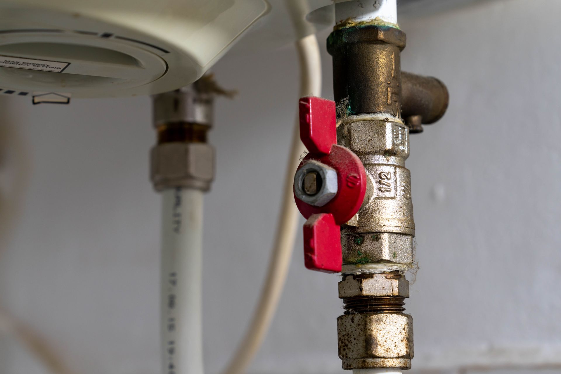 Red valve on a brass water pipe beneath a sink in a bathroom or kitchen