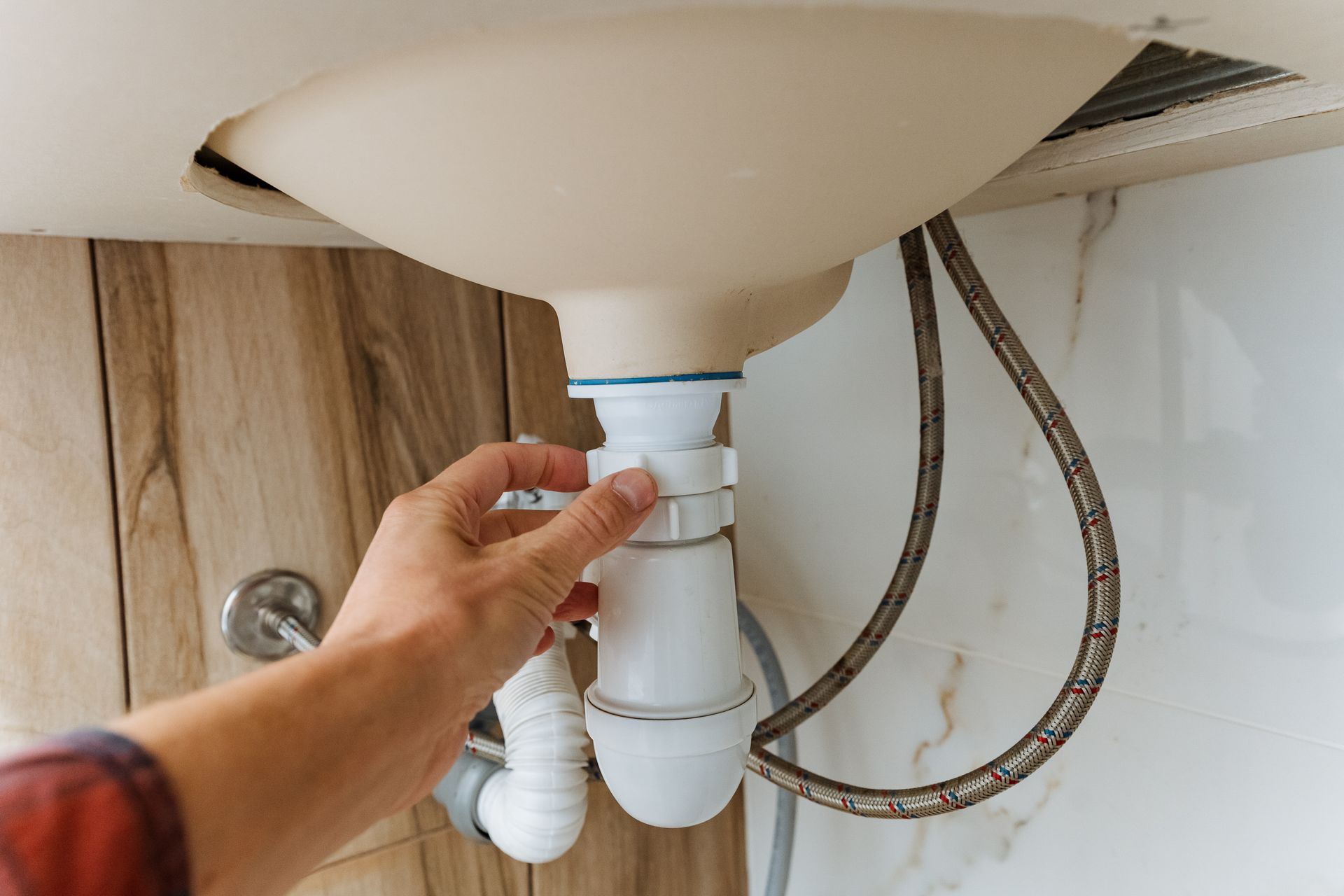Hand tightening a white sink drain pipe under a bathroom sink with exposed hoses.