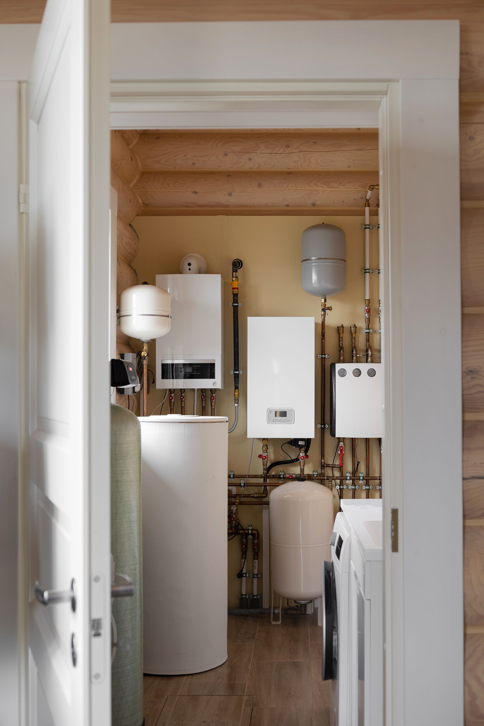 Utility closet with white plumbing tanks, pipes, and equipment on a wood floor