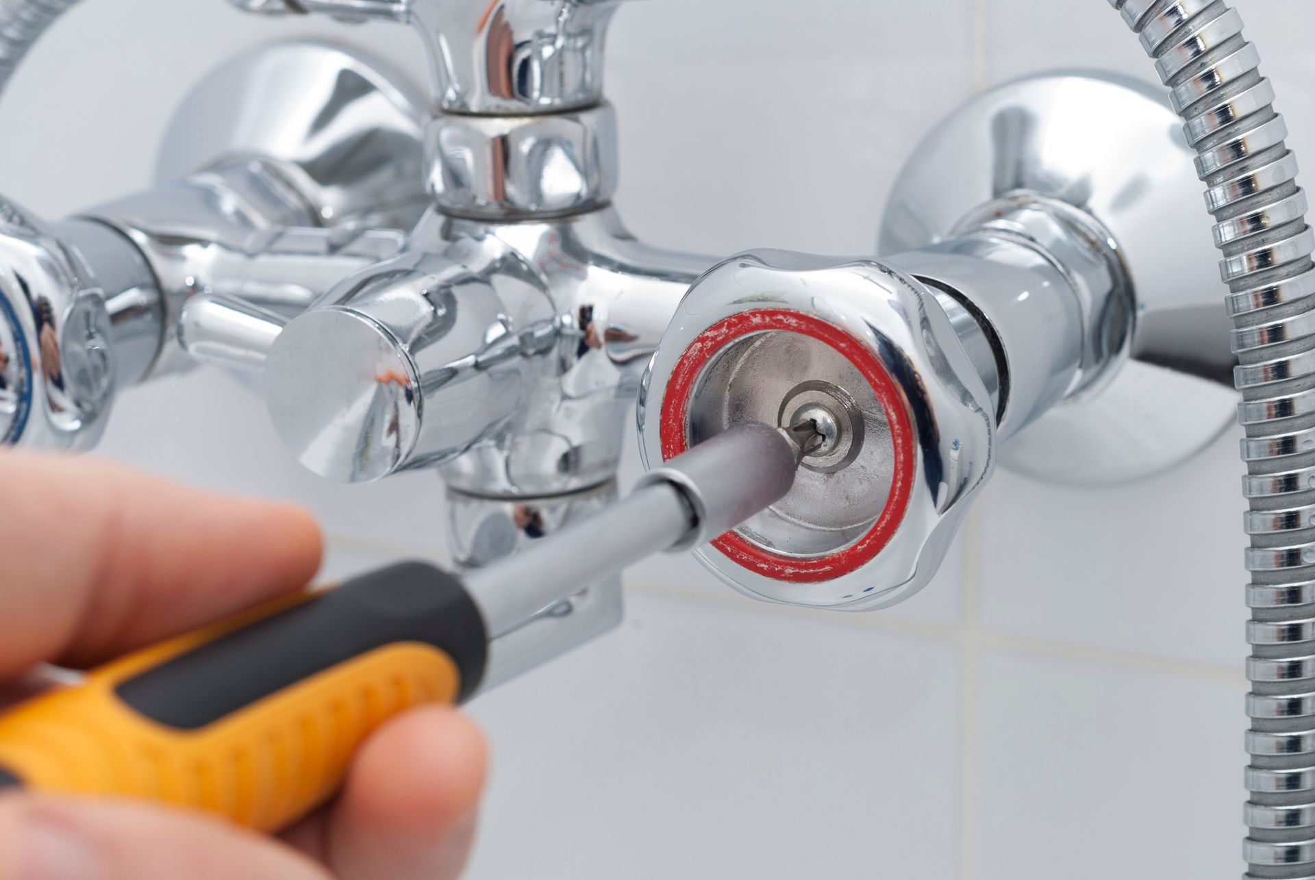 Person uses a screwdriver to adjust a chrome shower faucet valve.