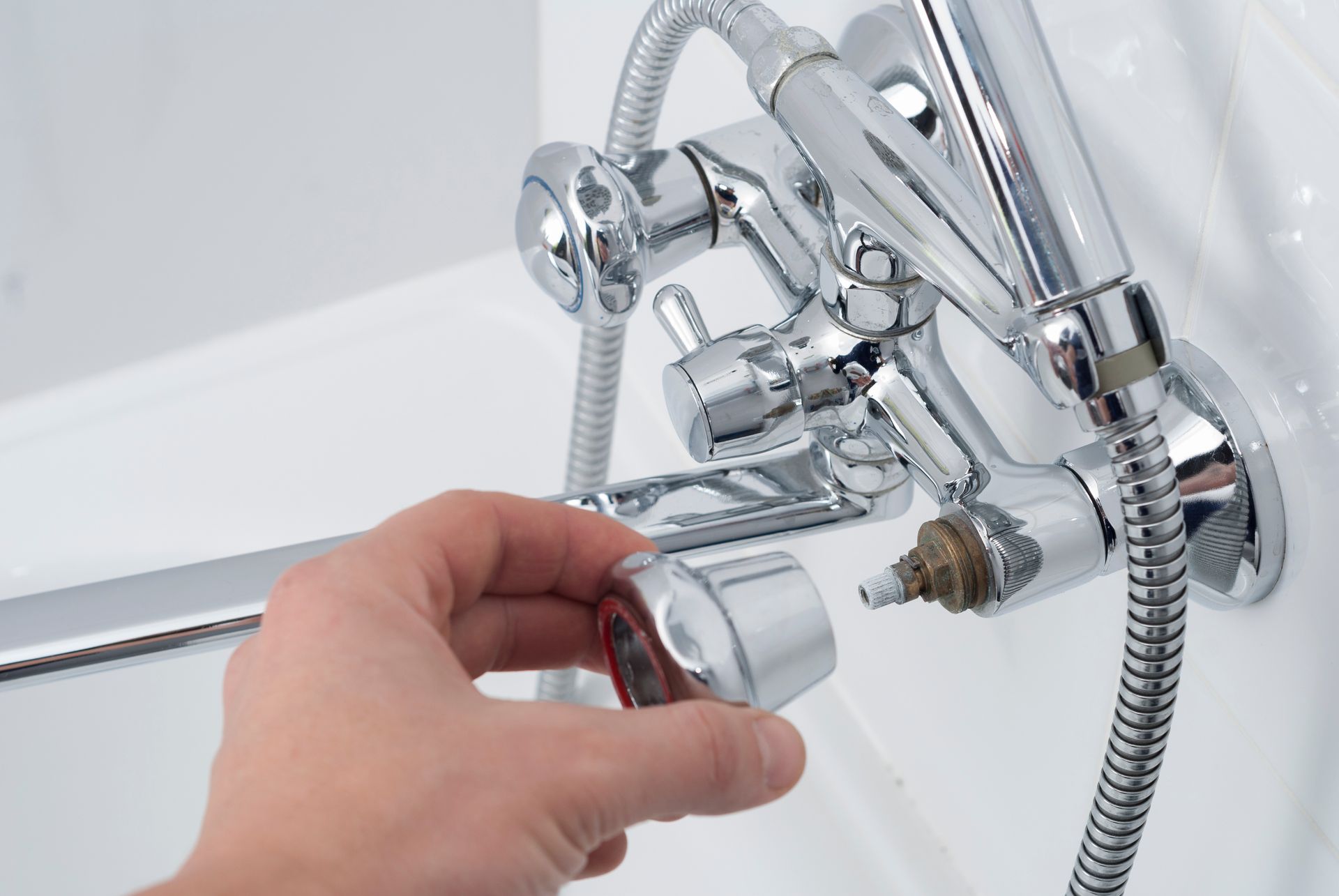Hand turning a chrome shower faucet knob in a white bathtub area