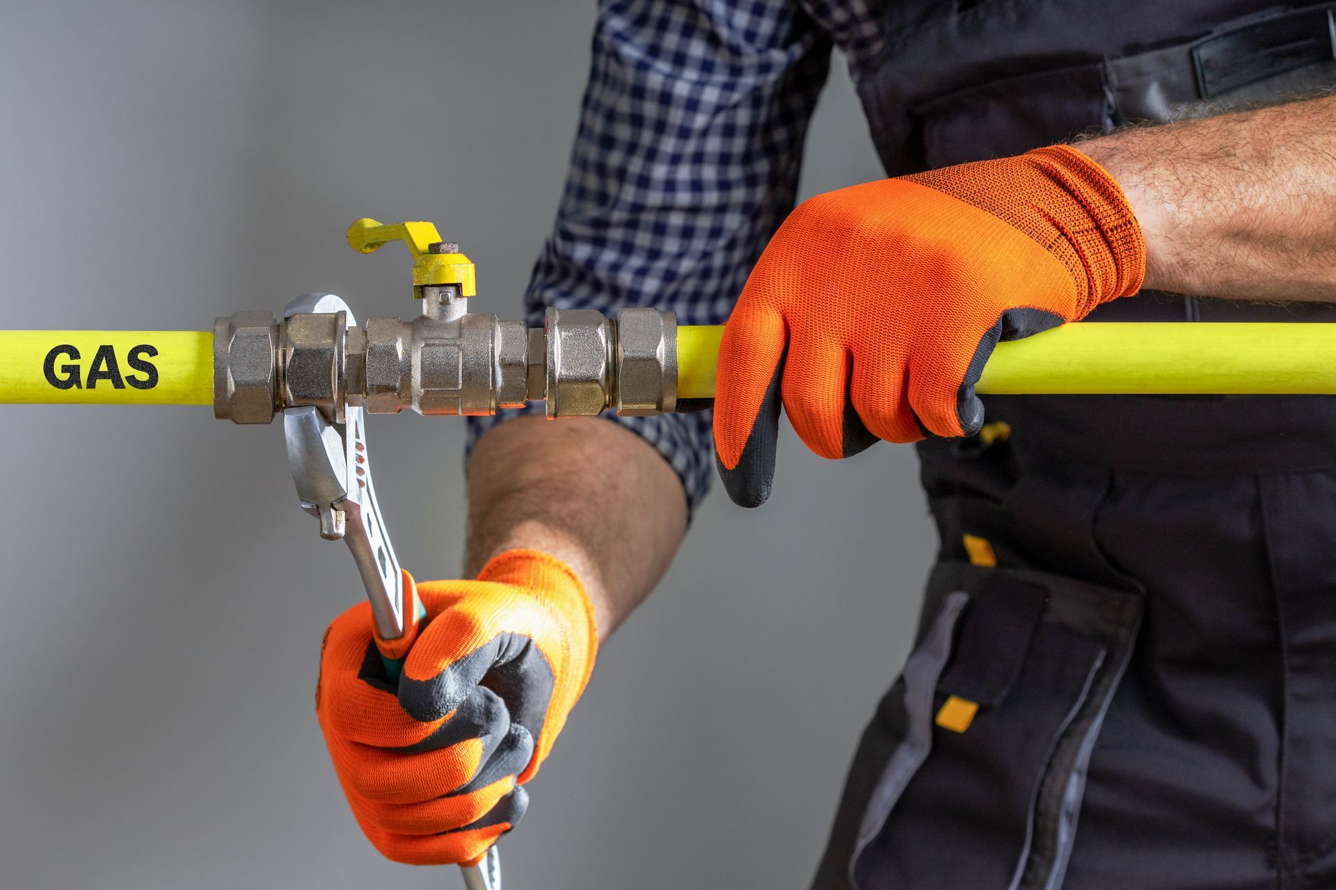 Gloved worker handling a yellow gas pipe with metal tools during maintenance