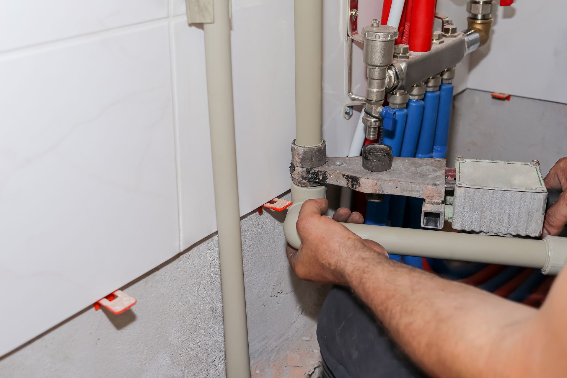Technician connecting pipes to a boiler manifold in a tiled utility room