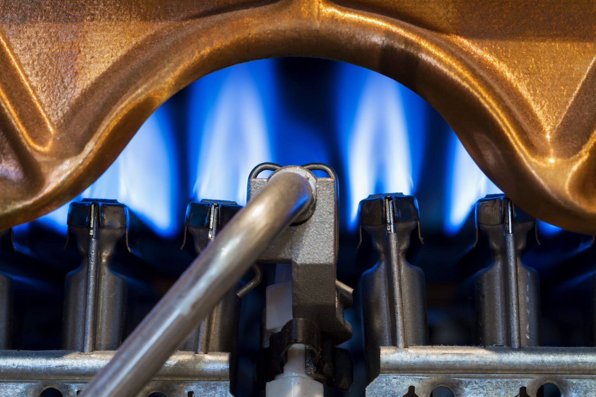 Blue gas flames beneath a metal burner assembly with a tool touching the center