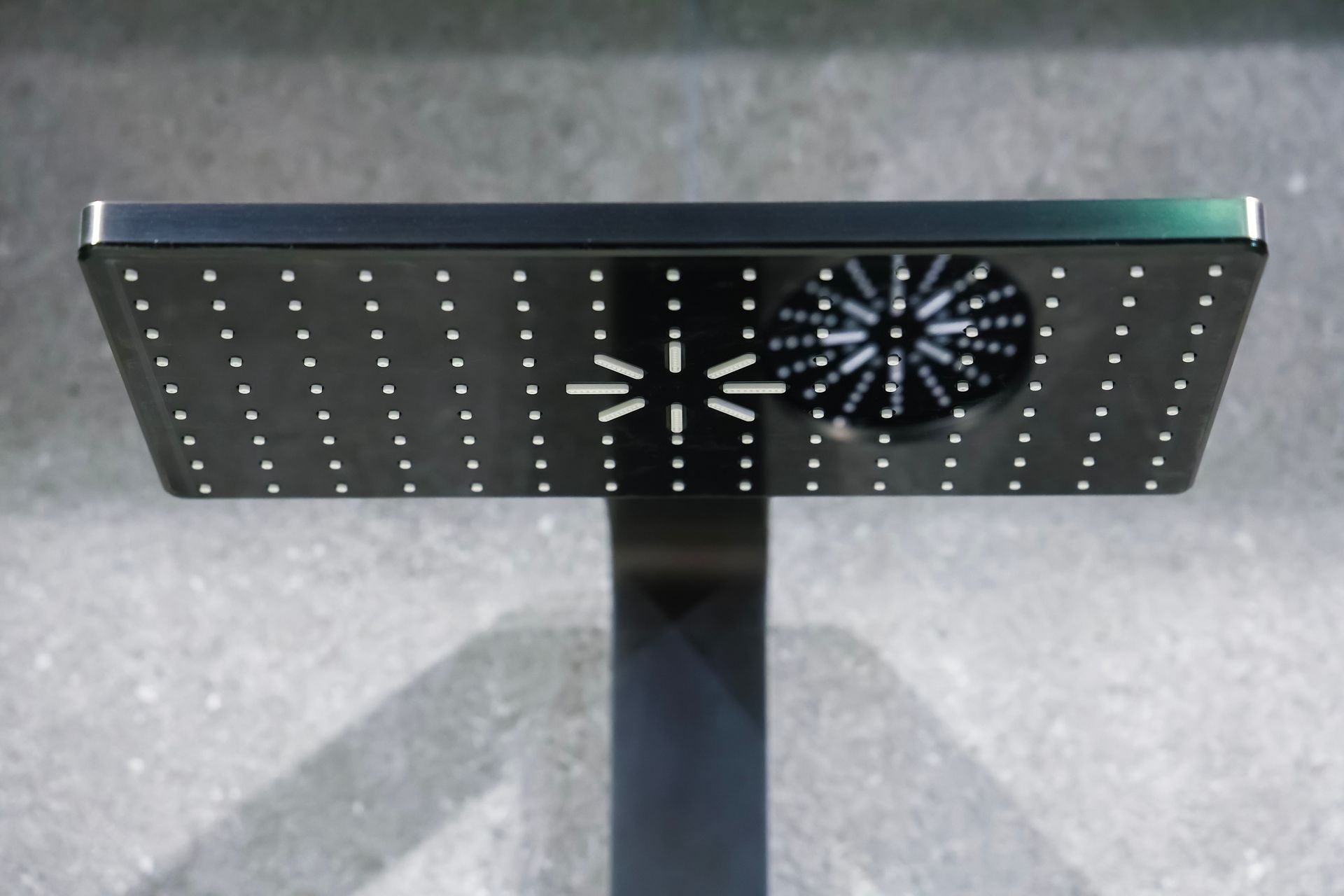Black perforated metal table with circular fan-like pattern on a gray floor