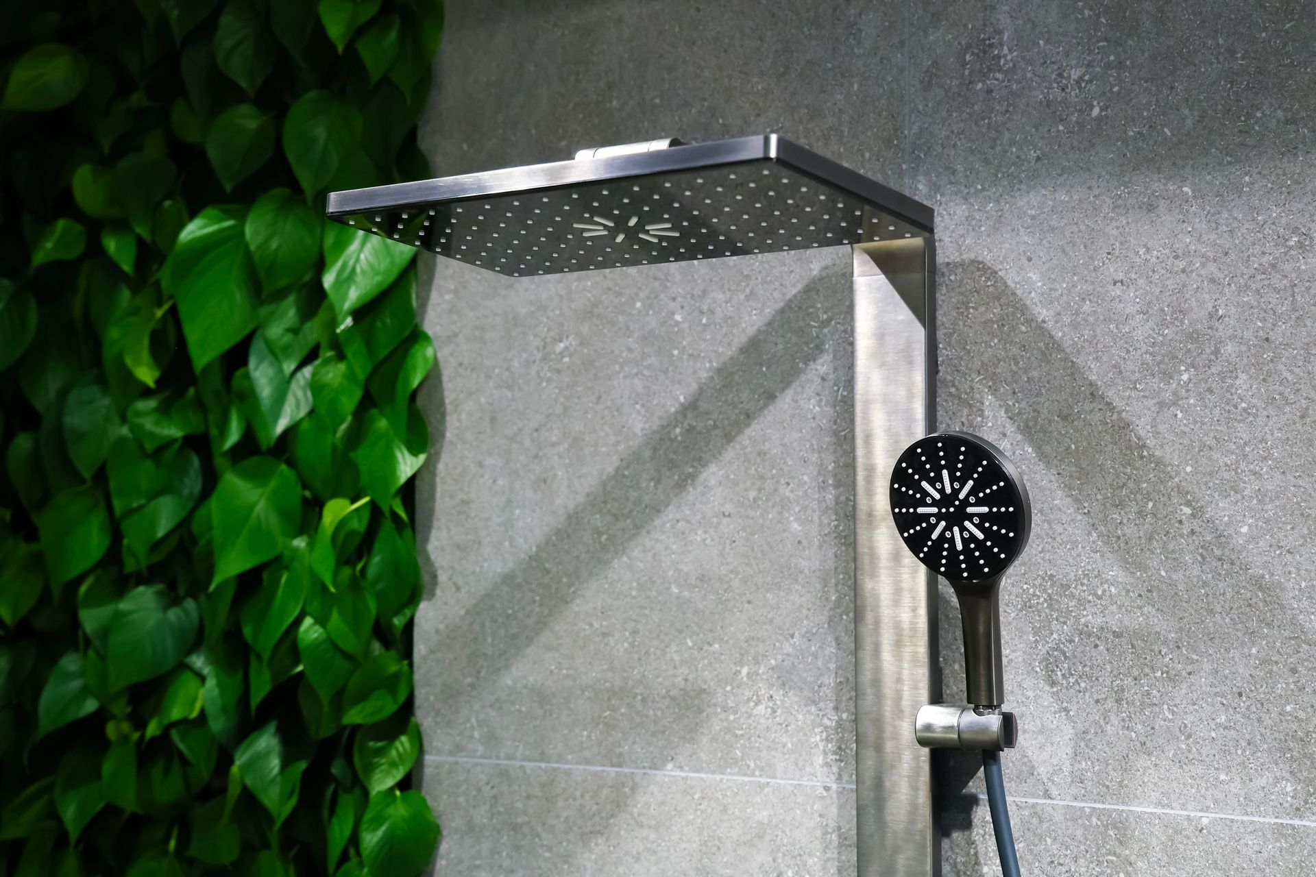 Modern shower with square rain head against gray tile and green leafy wall accent