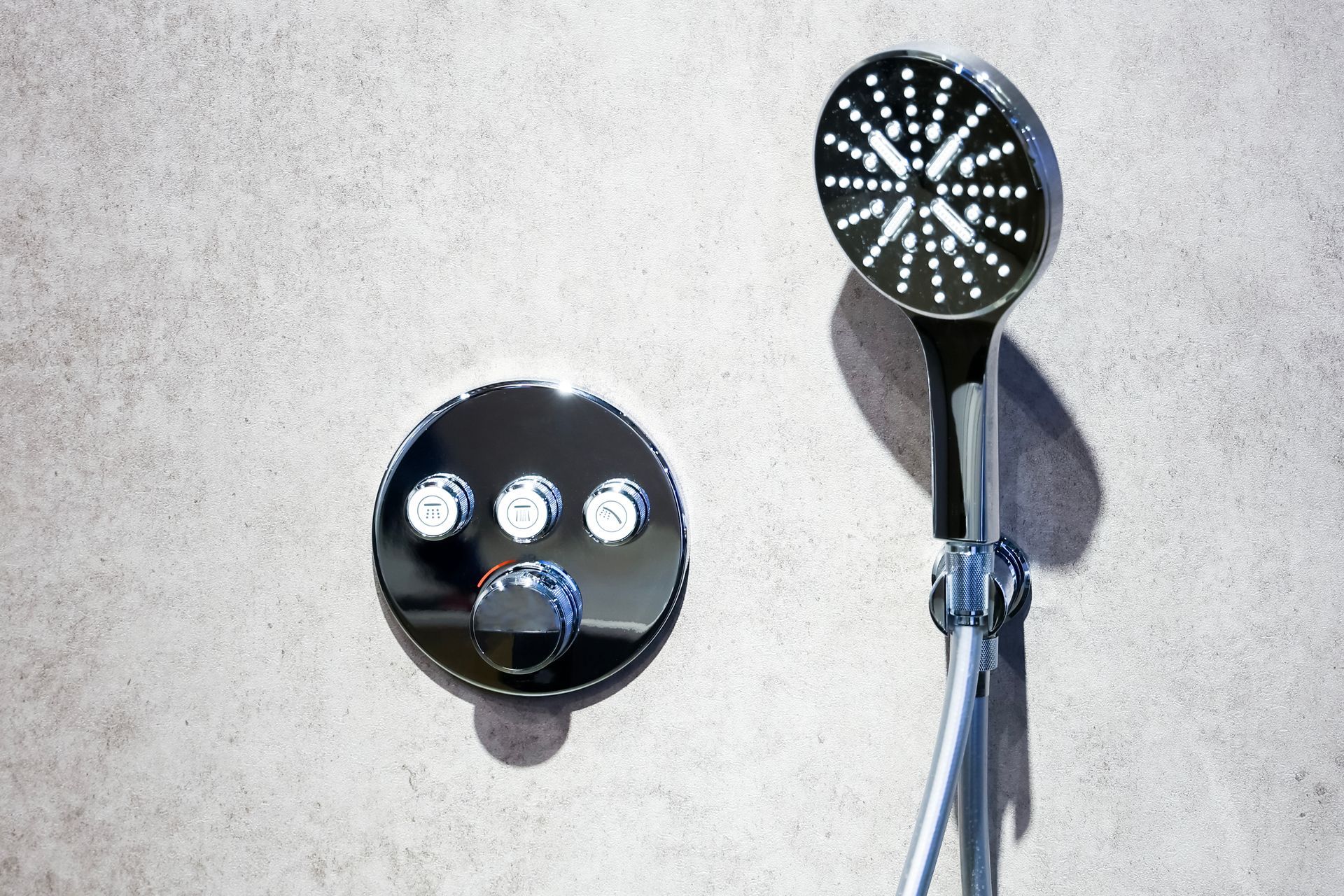 Black shower panel with two silver controls and a handheld showerhead on a light wall