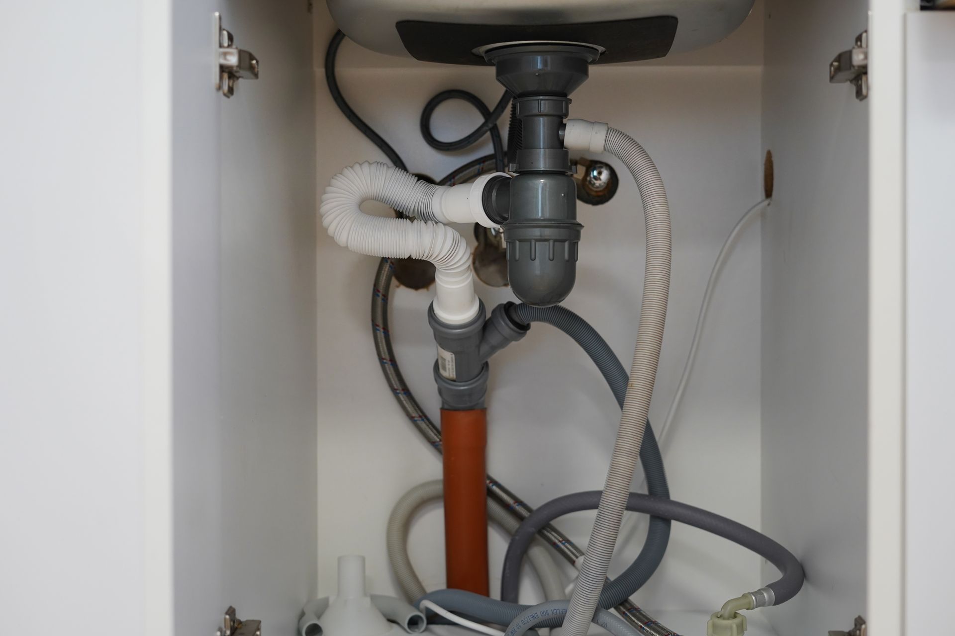 Under-sink cabinet plumbing with drain pipe, hoses, and exposed pipes.