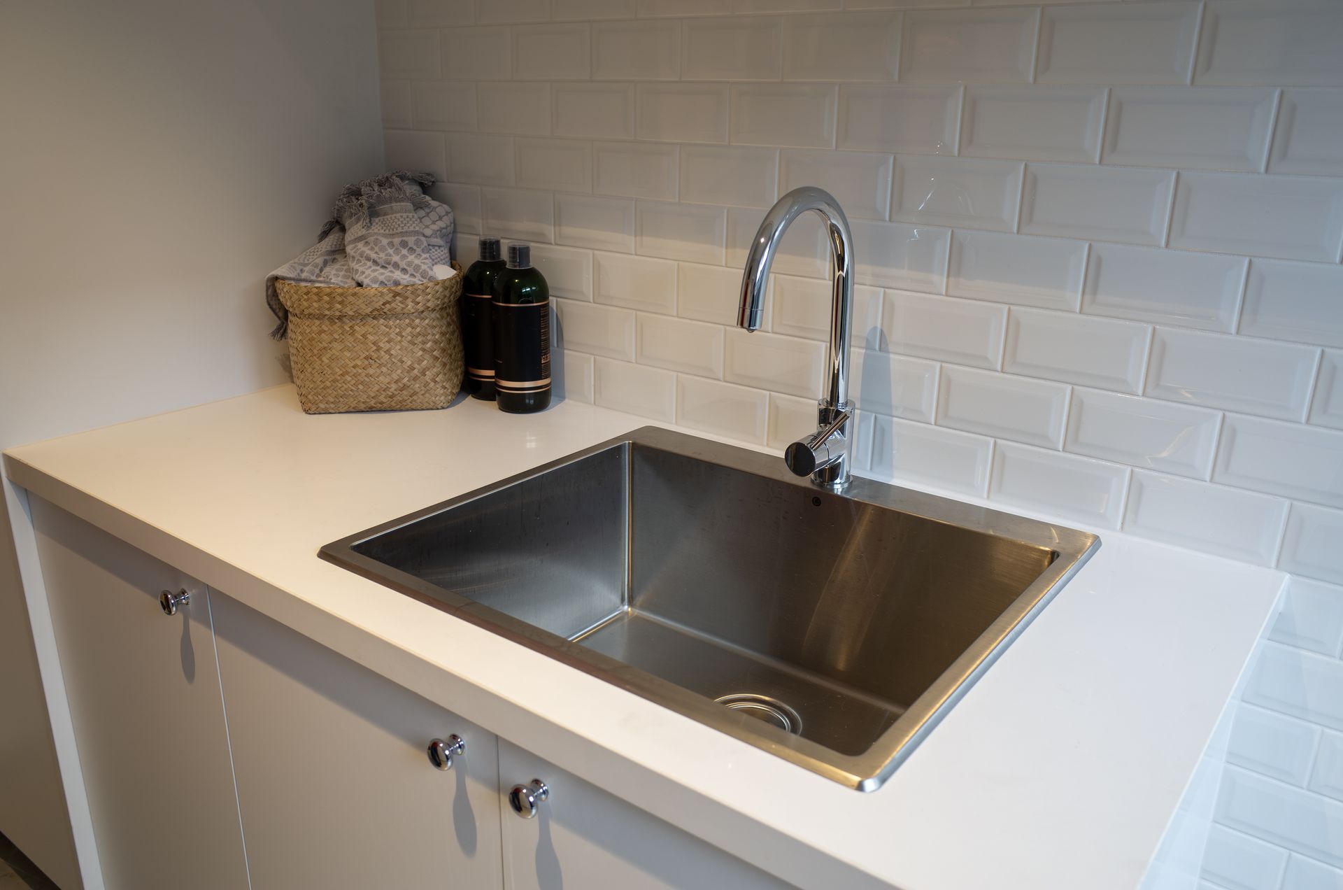 Modern kitchen sink with stainless steel basin, chrome faucet, white countertop, and white tile backsplash