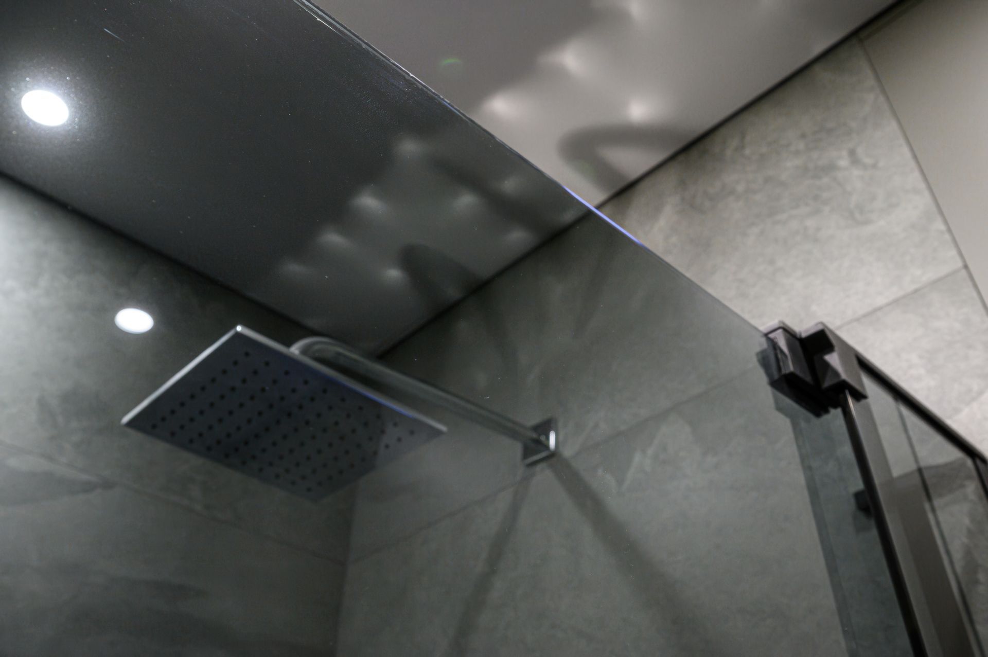 Modern tiled shower with square rainfall showerhead and glass enclosure