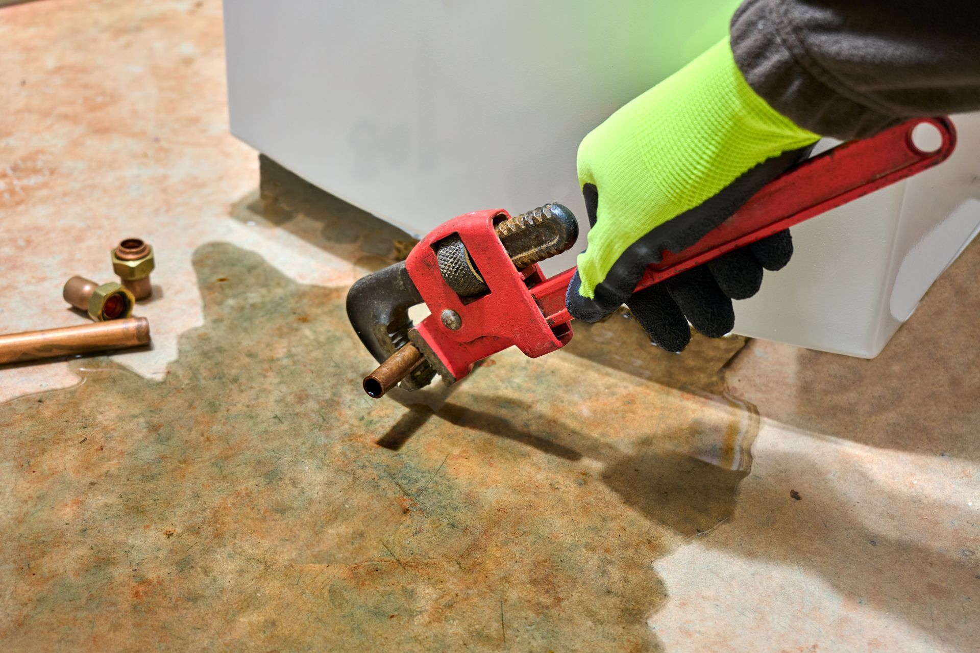 Gloved hand using a red caulking gun to apply sealant along a floor seam next to a white container
