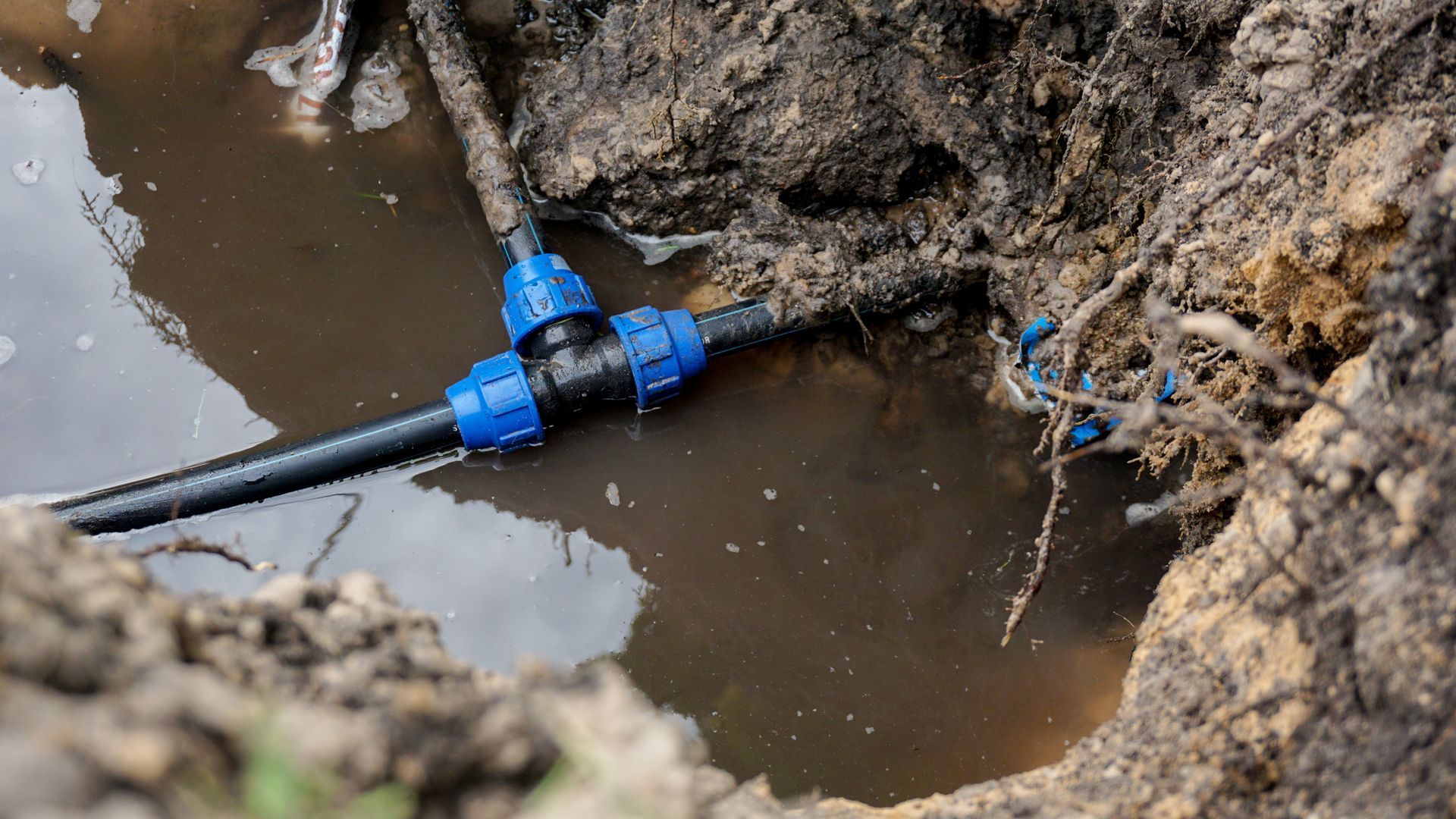 Blue pipe fitting repairing a leak in muddy trench water