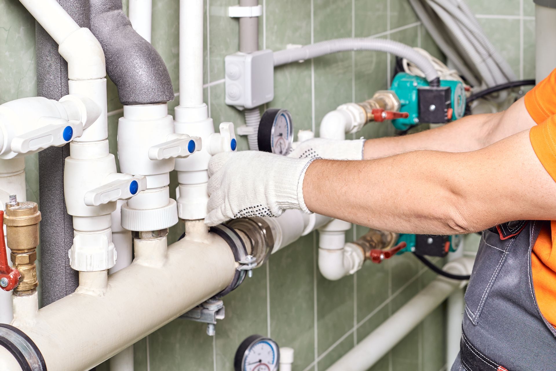 Technician tightening pipes on a plumbing manifold with tools in a tiled utility room